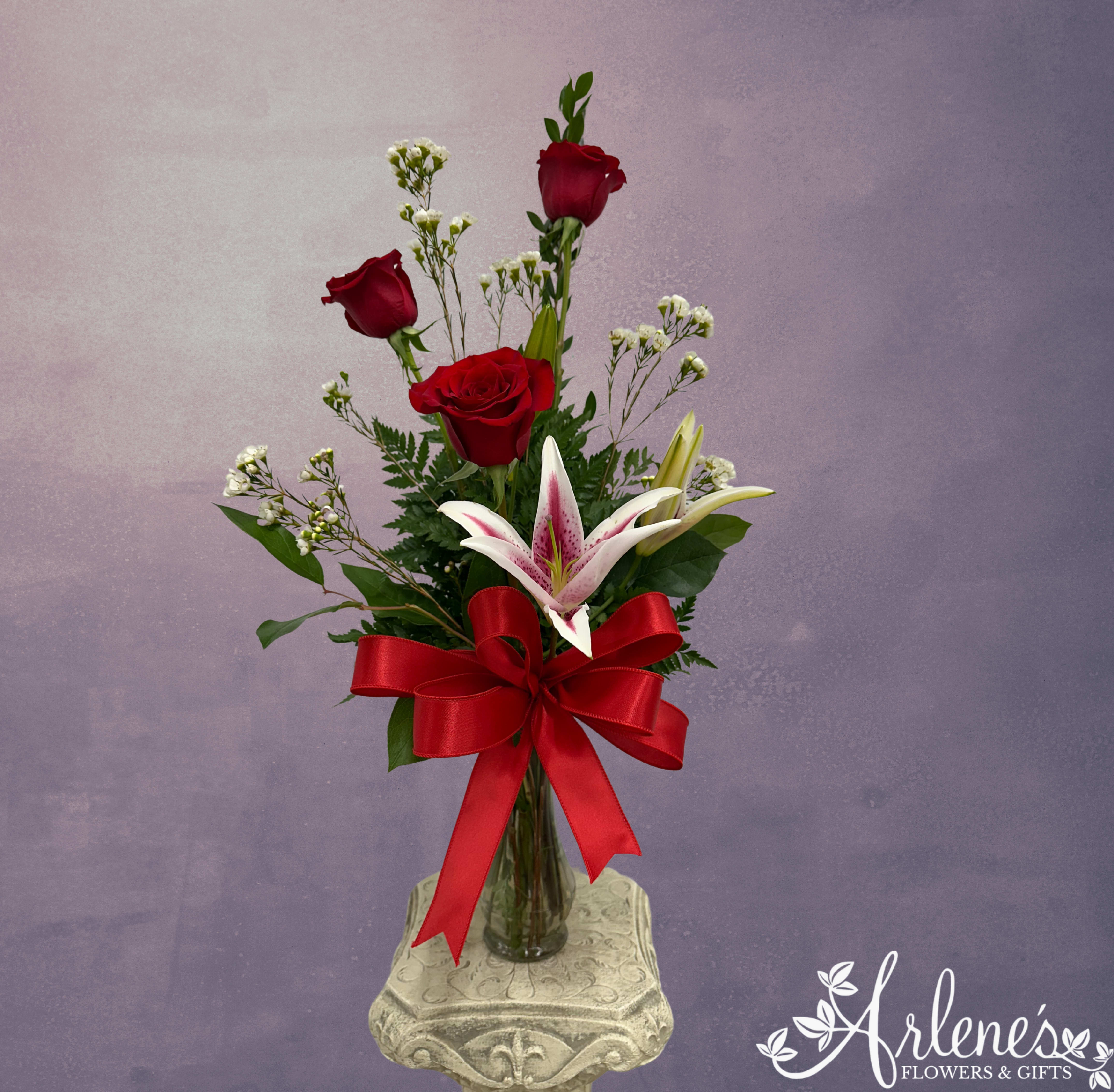 Rose Trio with Lilies - Affectionately known as the &quot;MiniRoll&quot; in the shop, this arrangement still hits the mark, but at a lower price point. Stargazer lilies and three red roses make this small stunner a powerful, sweet scented reminder that she is loved. 