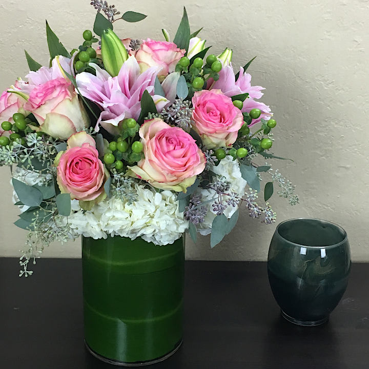 Spring Blooms - mixed pink and white roses and lilies surrounded by seasonal greenery in a glass vase accompanied with a ti leaf inside. 