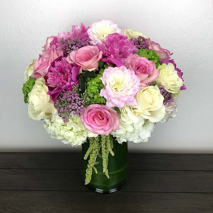 Spring Fling - a display of fun and flirtatious pink flowers complimented with whites and greens in a glass vase surrounded by a ti leaf