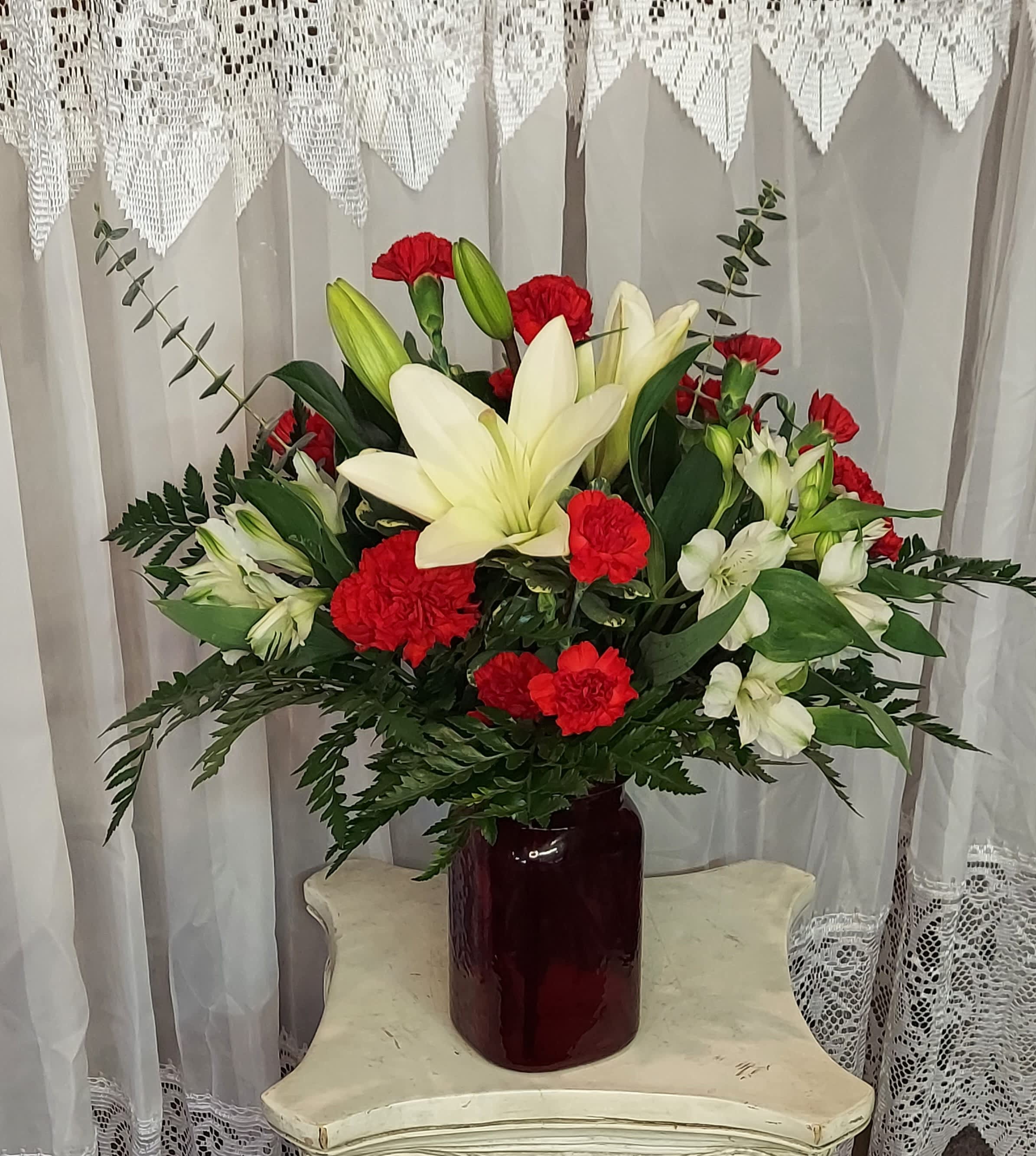 Forever Loved Forever Loved - A red and white tribute conveys the message that your loved one will never be far from your thoughts. Red carnations, mini carnations, white lily, and white alstroemeria in a red hammer jar. Approximate size: 17" H x 14"W