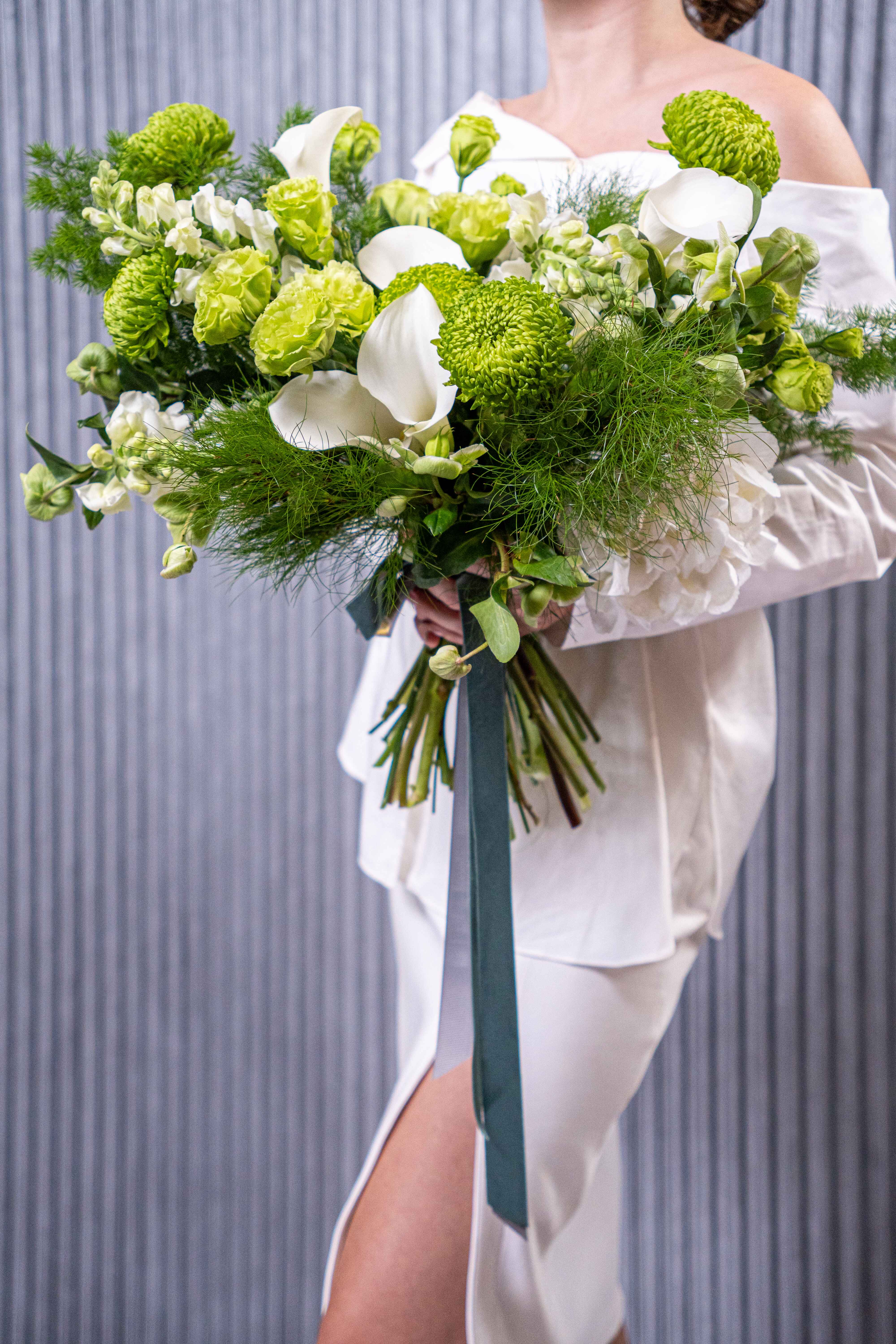 №203 Verdant Serenity - “Verdant Serenity” is an elegant and refreshing bouquet, featuring a sophisticated blend of white and green flowers. The White Calla Lilies, symbols of purity and grace, add a touch of sophistication, serving as a striking focal point with their sleek, elegant form. The combination of fresh green and pure white evokes a sense of harmony and tranquility. This bouquet radiates a natural, serene beauty, making it perfect for occasions that require an understated yet striking floral arrangement. “Verdant Serenity” effortlessly conveys freshness, balance, and elegance.