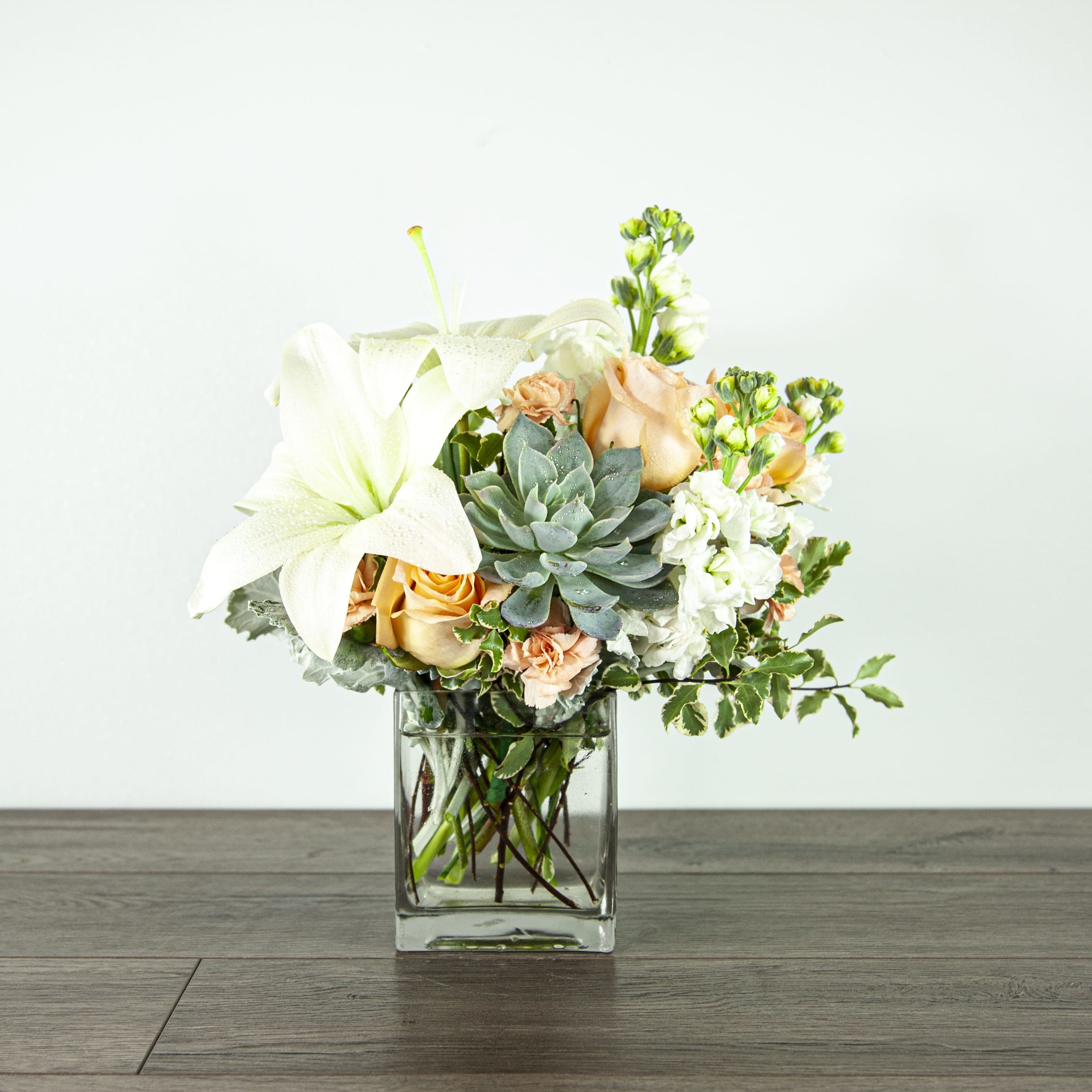 Desert Sunrise (EXP 61-B) - This pastel-colored arrangement is a wonderful way to show your love and appreciation to that special someone.   Blooms in this arrangement: - 3 peach roses - 1 white Asiatic lily - 2 peach mini carnation stems - 3 white stock stems - 1 four inch succulent