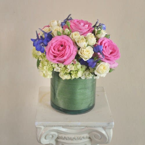 Sincerely Yours - Pink Roses, Blue Delphinium, White Hydrangea and Pale Yellow Spray Rose in Leaf lined cylinder vase