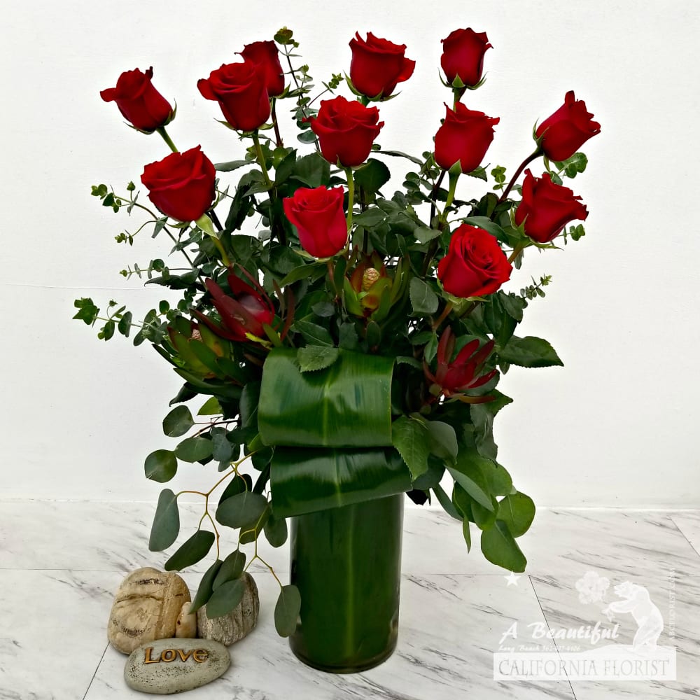 Modern Romance - Red Roses Modern Romance - Red Roses - Modern Romance, this is the updated and enhanced version of our Classic Romance. One Dozen beautiful RED long stem roses arranged in a tall cylinder vase. Accents of exotic red safari, spiral and silver dollar eucalyptus, verdant ti leaves upgrade and transport this time tested declaration of love to the present. Modern Romance from your favorite five 5 star Long Beach Flower shop, A Beautiful California Florist