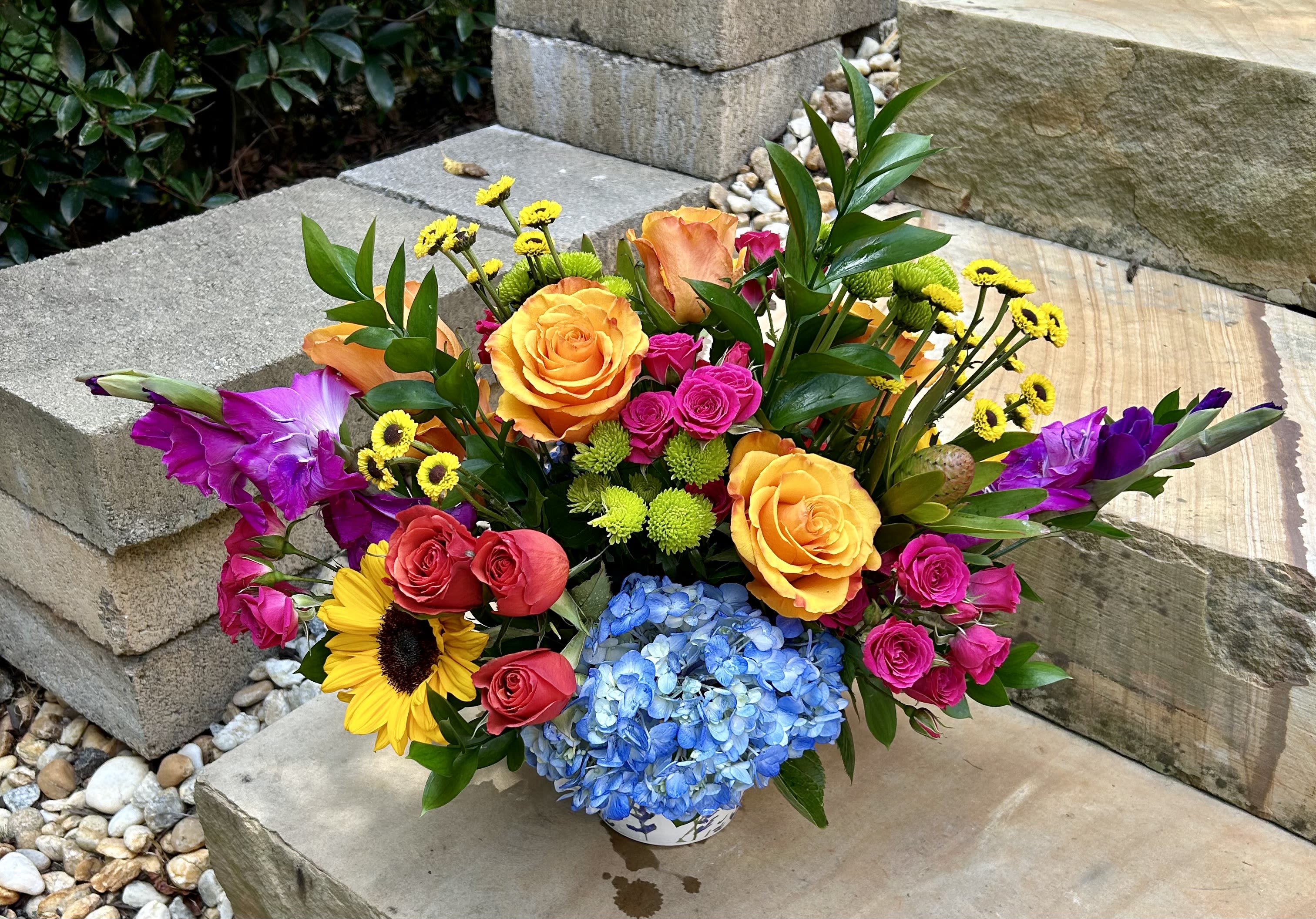 Rainbow of Colors - A ceramic pot of flowers that includes sunflowers, roses, spray roses, gladiolus, hydrangeas and fillers in all different colors to mimic the rainbow.