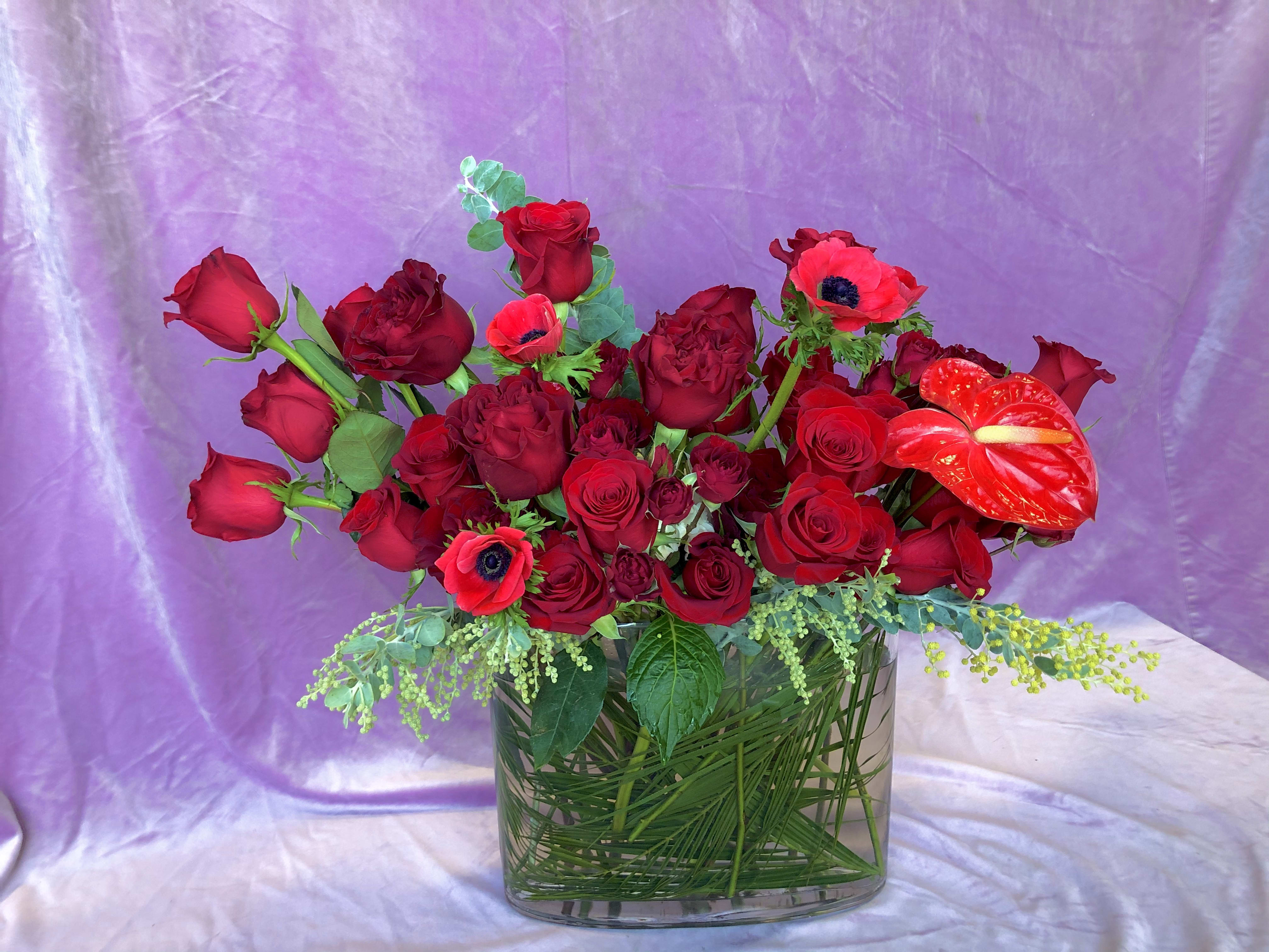 Romeo - Variety of red premium blooms in a clear glass 12&quot; oval vase. This full and lush large designer's choice Valentine's Day arrangement is hand crafted in Las Vegas by our all-women design team using the freshest red roses and red garden roses from around the world.