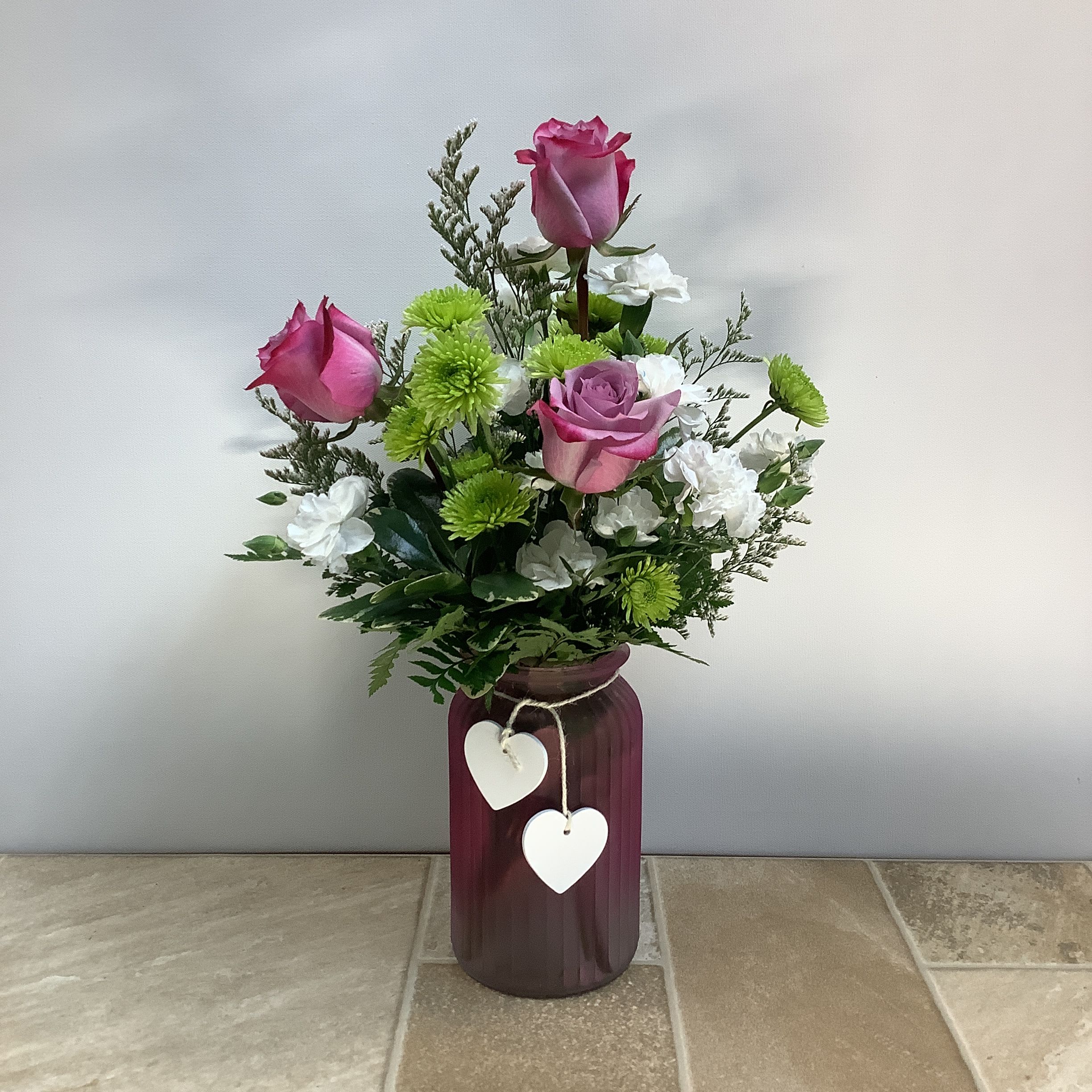 Sweet Lilac Sweet Lilac - A delightful gathering of lavender roses, green athos and mini carnations in a pretty glass vase. It measures 11” x 18” tall.