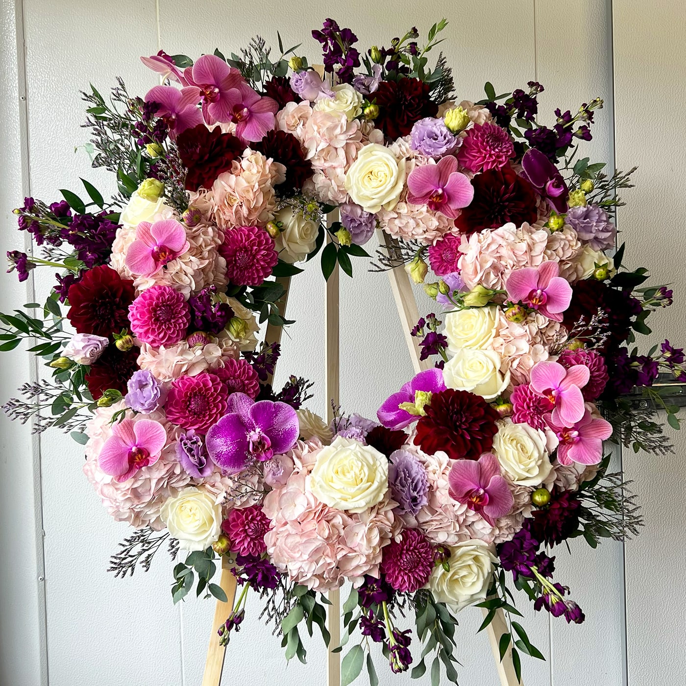 PURPLE N PINK WREATH - purple, pink, white flowers, and greenery. The standing cross includes the wood easel.  Pink roses, white hydrangeas, spray roses, orchids, seasonal florals, and greenery