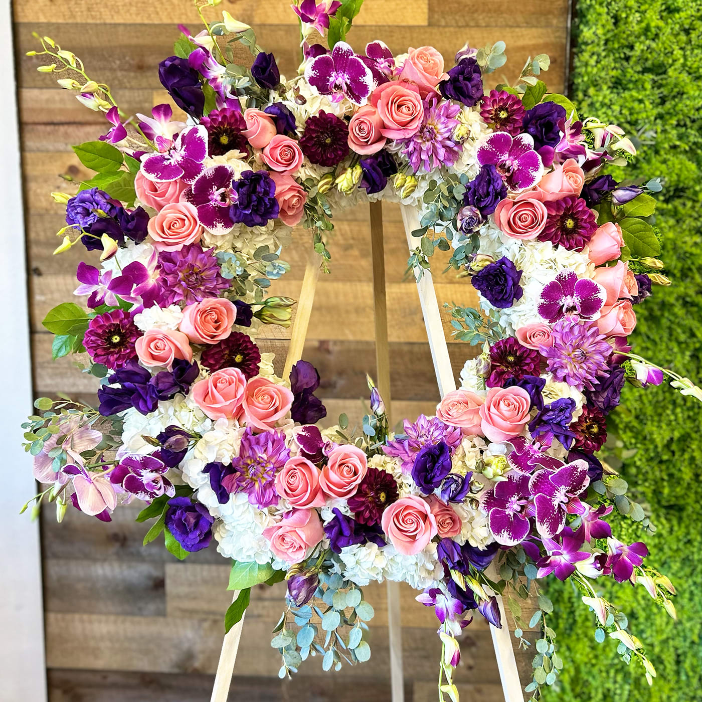 PURPLE, PINK, N WHITE WREATH - purple, pink, white flowers, and greenery. The standing cross includes the wood easel. Pink roses, white hydrangeas, spray roses, orchids, seasonal florals, and greenery