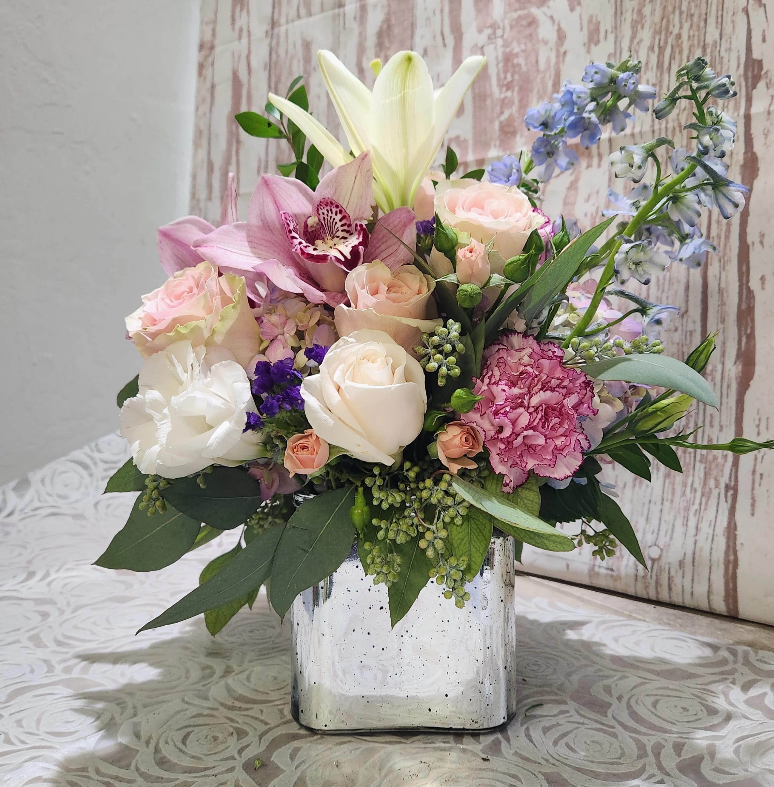  Garden Of Dreams Bouquet - Make her dreams come true with this bouquet presented in a silver cube or cylinder style vase mixed with lavender and white seasonal blooms white lilies lavender roses blue delphinium ,  Will be delivered a cube or cylinder vase.  (VASE  MAY VARY due to availability) it's an elegant choice for weddings, showers, birthdays. Standard will be one side Deluxe size is all around  Pictured is a Deluxe Size      