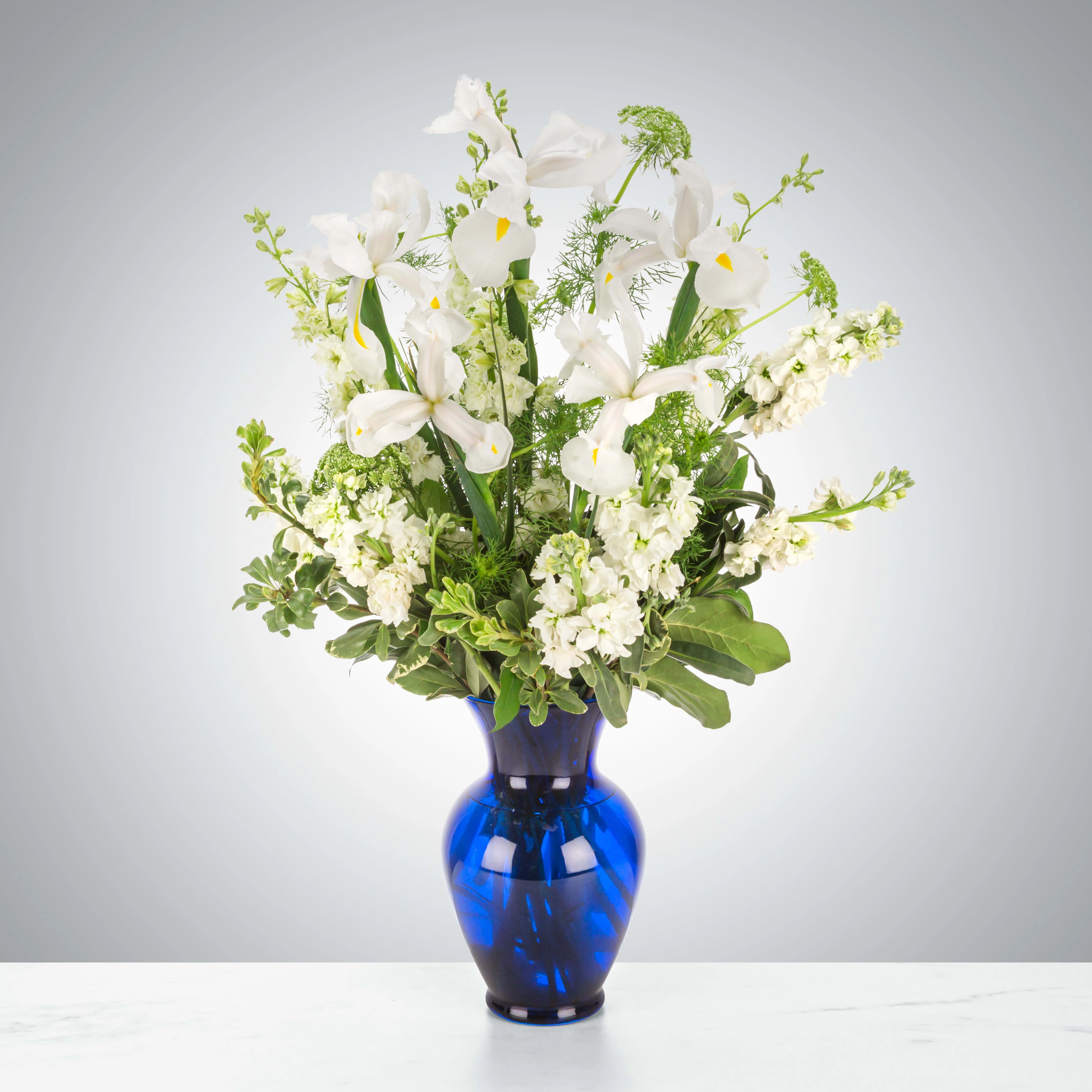 Crystal Symphony - This arrangement includes white iris, white stock, white snapdragons, and queen anne's lace in a blue vase. Send your condolences with Crystal Symphony 