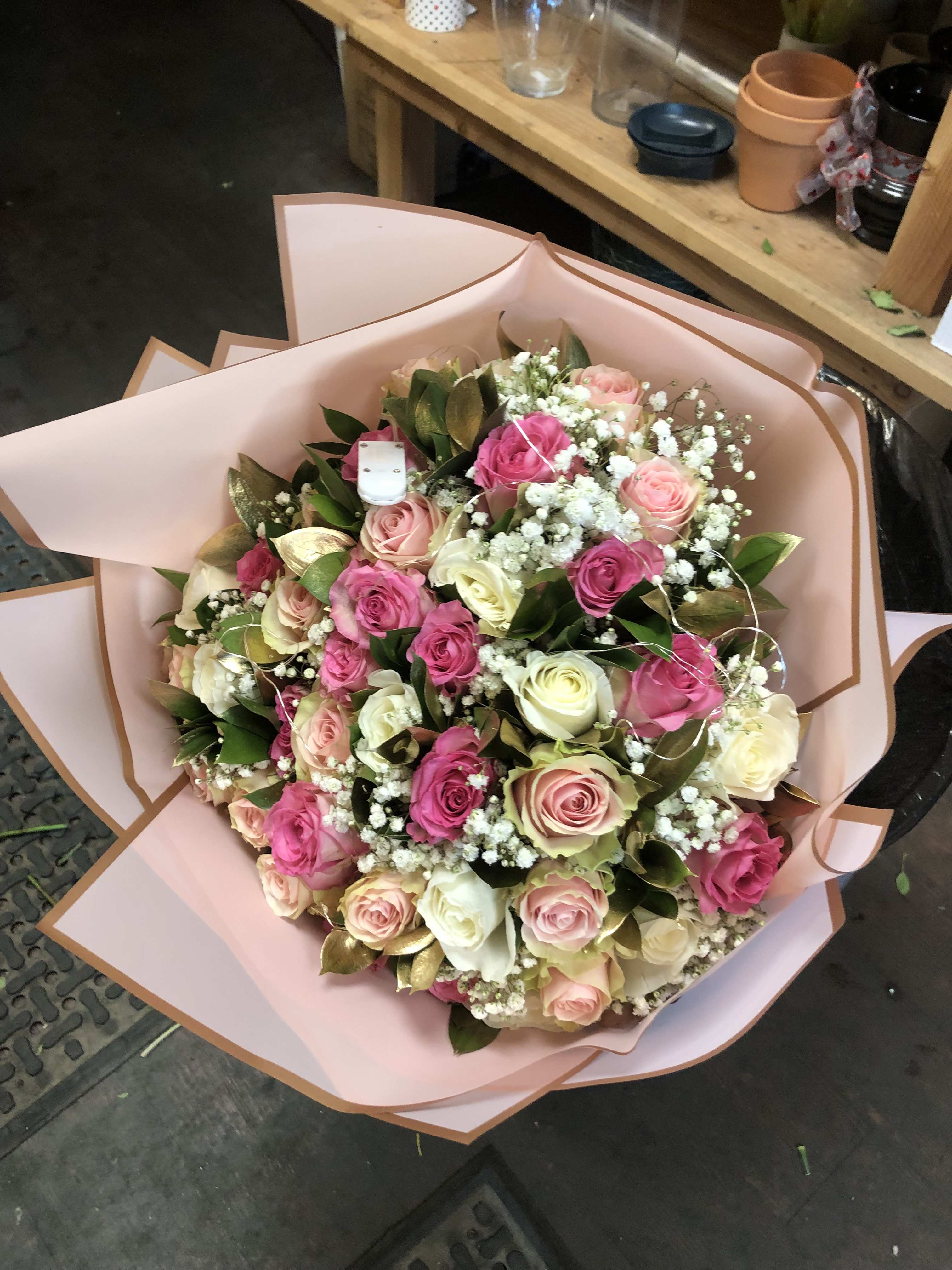 CUPID MELODY (WRAP) CUPID MELODY (WRAP) - 16 Pink Roses, 16 Off white Roses, 16 Light pink Roses, with baby breath and gold ruscus leaves all wrapped in Korean paper. This arrangement has fairy lights. 50 ROSES total