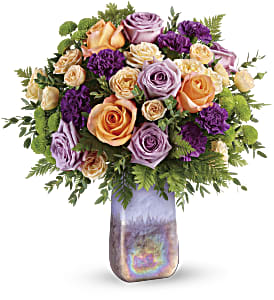 Amethyst Sunrise Bouquet - Two gifts in one! This glorious bouquet of lavender and peach roses is arranged in a hand-blown art glass vase, a shimmering, iridescent gift they'll treasure forever. This glorious bouquet includes lavender roses, peach roses, peach spray roses, purple carnations, green button spray chrysanthemums, leatherleaf fern, and parvifolia eucalyptus. Delivered in an Amethyst Gemstone Art Glass vase. Approximately 18 1/4&quot; W x 19 1/4&quot; H