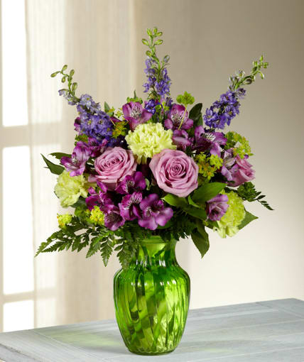 Beautiful Expressions Bouquet - Captivate your recipient with the graceful beauty of this arrangement featuring lavender roses surrounded by green carnations, purple larkspur, purple Peruvian Lilies, bupleurum, and a variety of lush greens in a green swirled glass vase.