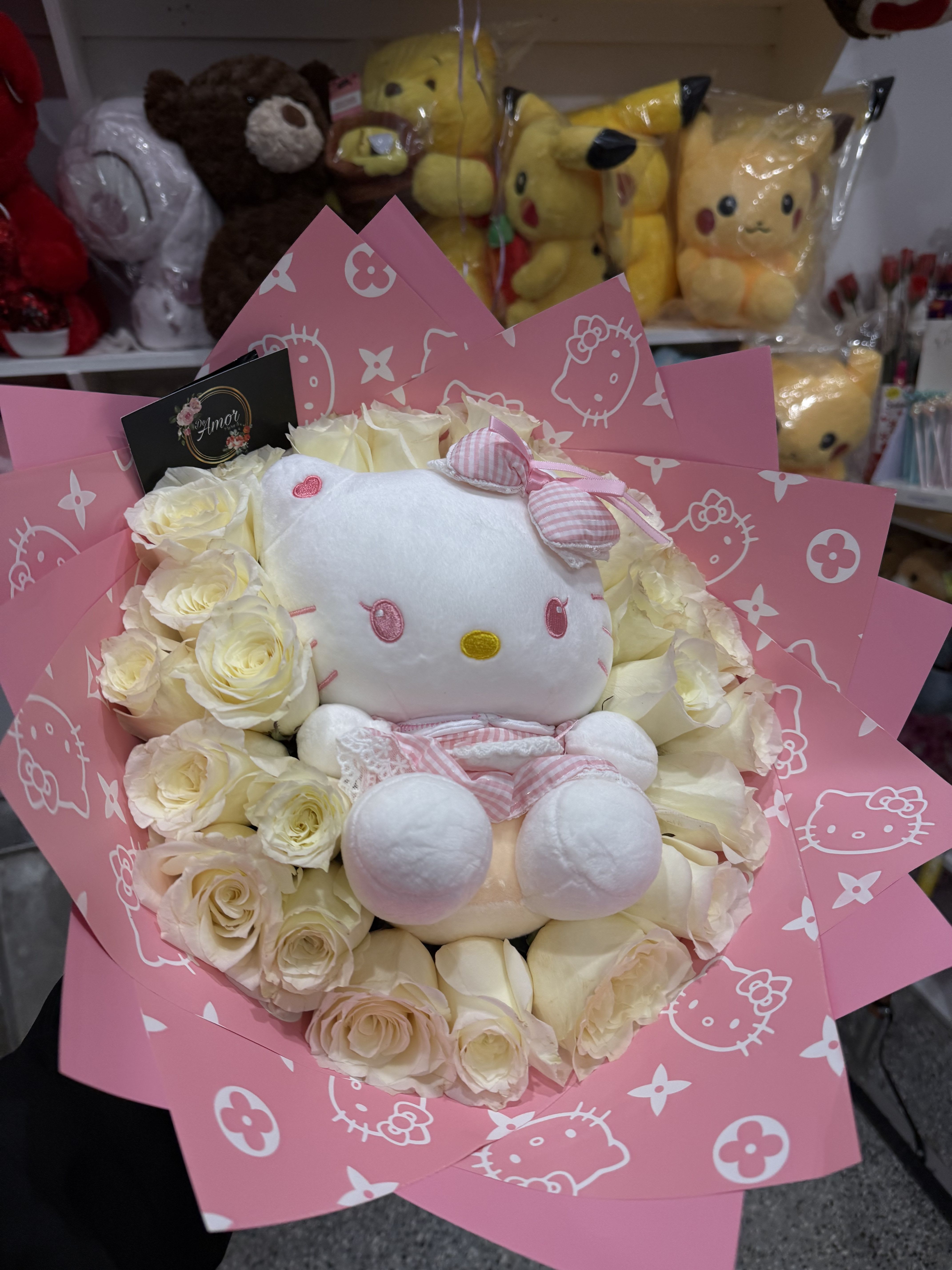 Hello Kitty Mini Bouquet Hello Kitty Mini Bouquet - A beautiful bouquet of white roses encircles a Hello Kitty plush toy, creating a charming and sweet gift arrangement. The bouquet is composed of 25 white roses tightly arranged around the Hello Kitty plush toy. The plush toy is centrally located and prominently displayed, dressed in a light pink and white outfit. The roses are neatly arranged in layers, filling the container, and the pink wrapping paper with a Hello Kitty design adds to the overall aesthetic. The wrapping paper has a repeating pattern of Hello Kitty faces and old newspaper monogram print in white. The arrangement is visually appealing and designed for gifting. The artistic medium is a floral bouquet design with a plush toy, showcasing a combination of natural elements (roses) and a soft plush toy. The execution is meticulous, with the roses arranged to showcase the Hello Kitty plush toy. The color palette is limited to shades of pink and white, creating a delicate and feminine feel. The design style appears to be a modern twist on a classic floral arrangement.