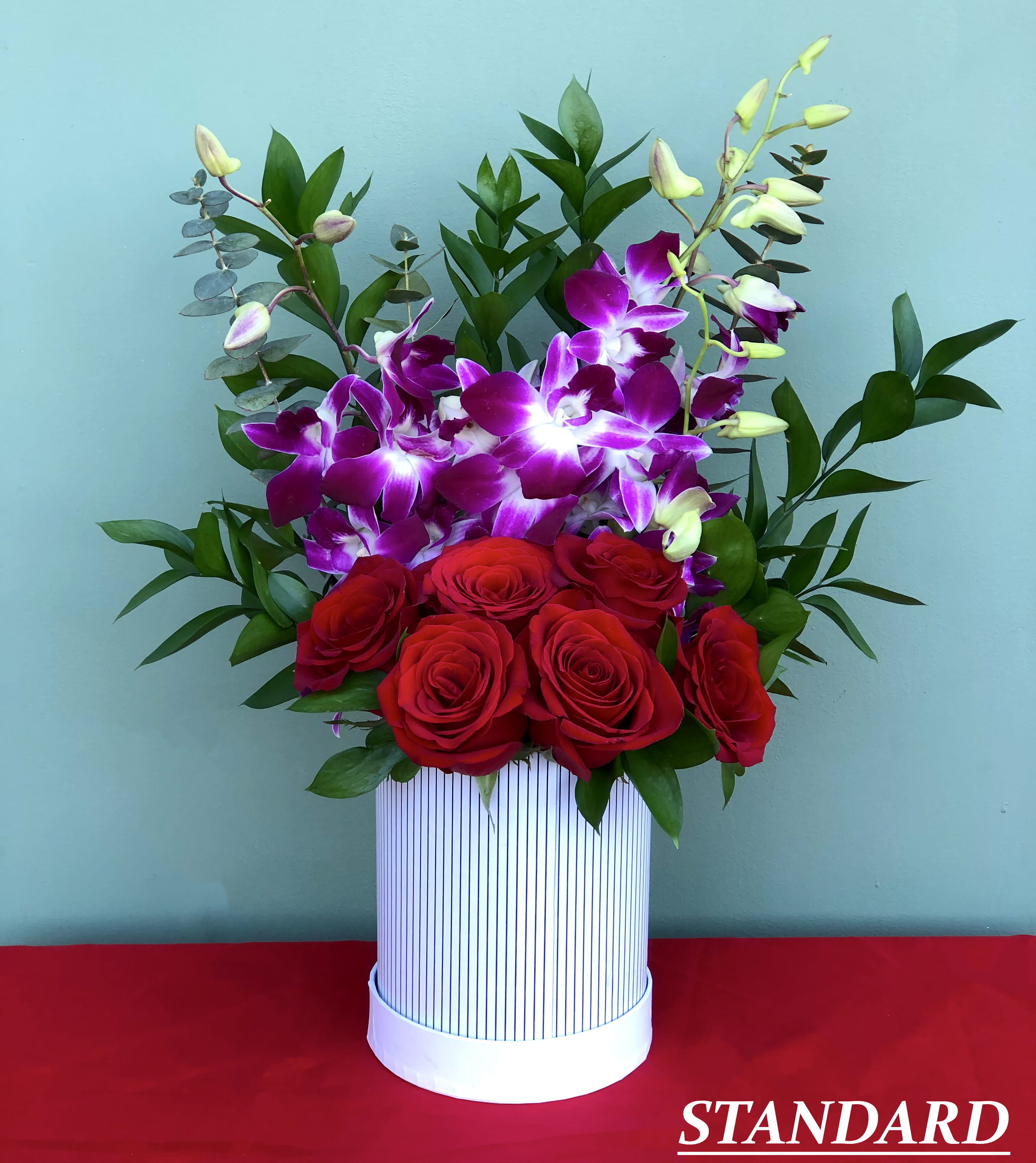 Pure Love - This charming arrangement combines the classic beauty of red roses with the bold colors of dendrobium orchids, eucalyptus and Israeli ruscus   Approximate dimensions: Standard: 7&quot; Wide and 15&quot; High Deluxe: 10&quot; Wide and 22&quot; High Deluxe: 10&quot; Wide and 22&quot; High