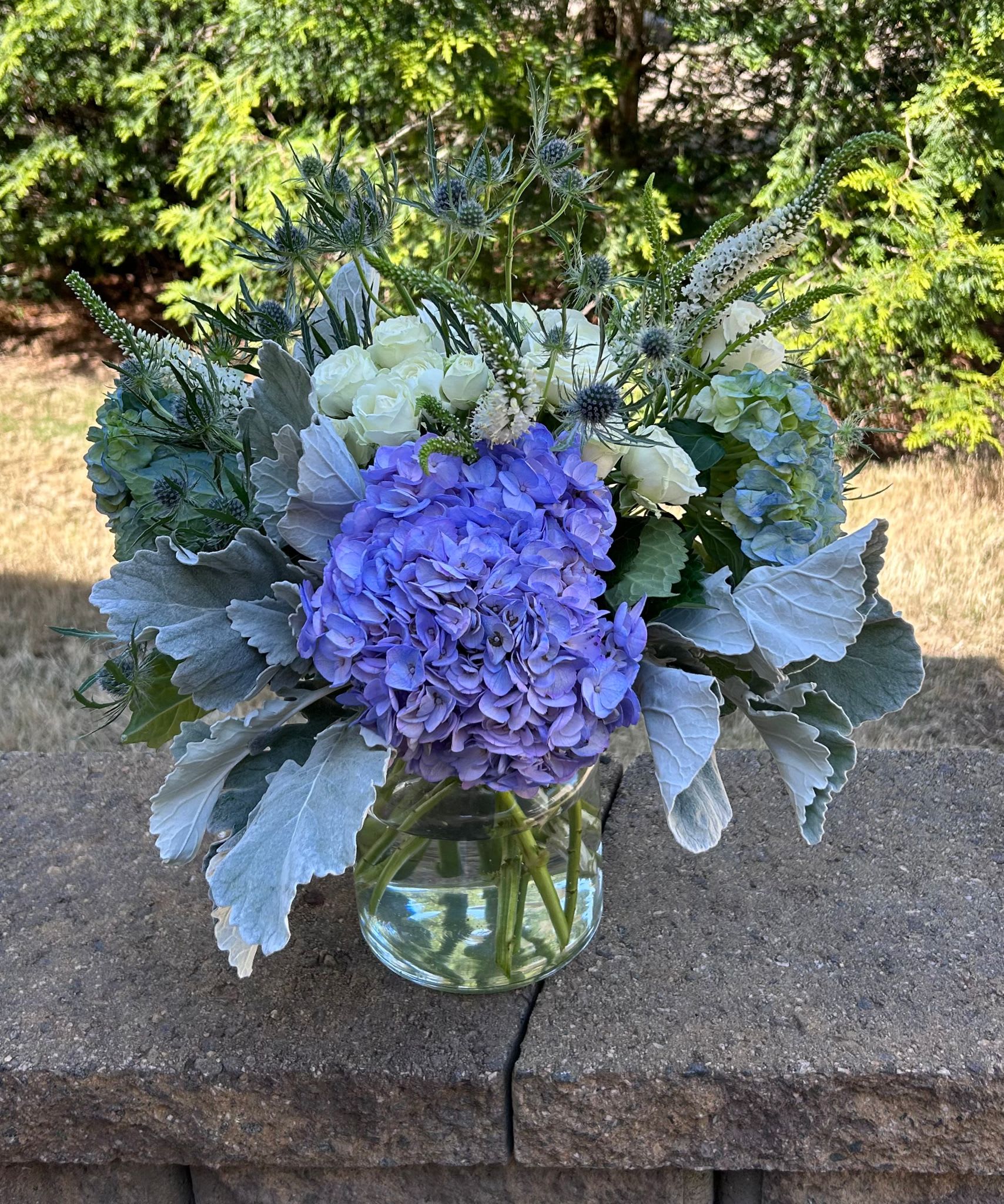Royal Blue Bouquet - A beautiful Royal Blue Bouquet that adds a touch of elegance and sophistication. Bloom Details: White Spray Roses, Blue Dark Hydrangea, Thiesel, White Veronicas, Dusty Miller Clear Glass All Occasion Place your Order Online Monday to Saturday before 1:00 p.m. (E.T.) for same-day delivery. “Orders received after hours will be delivered the next business day”. Check our coverage area. Occasionally, flowers and/or container substitutions happen due to weather, seasonality, and market conditions, which may affect availability. If this is the case with the gift you’ve selected, we will ensure that your arrangement's style, theme, and color scheme are preserved and will only substitute items of equal value or higher value.  CARE INSTRUCTIONS Keep the flower arrangement hydrated with natural water and change the water every two days. Do not spray any cleaning product on the flower arrangement. Do not place heavy objects directly on the flower arrangement. Keep flower arrangements out of direct sunlight and extreme heat.