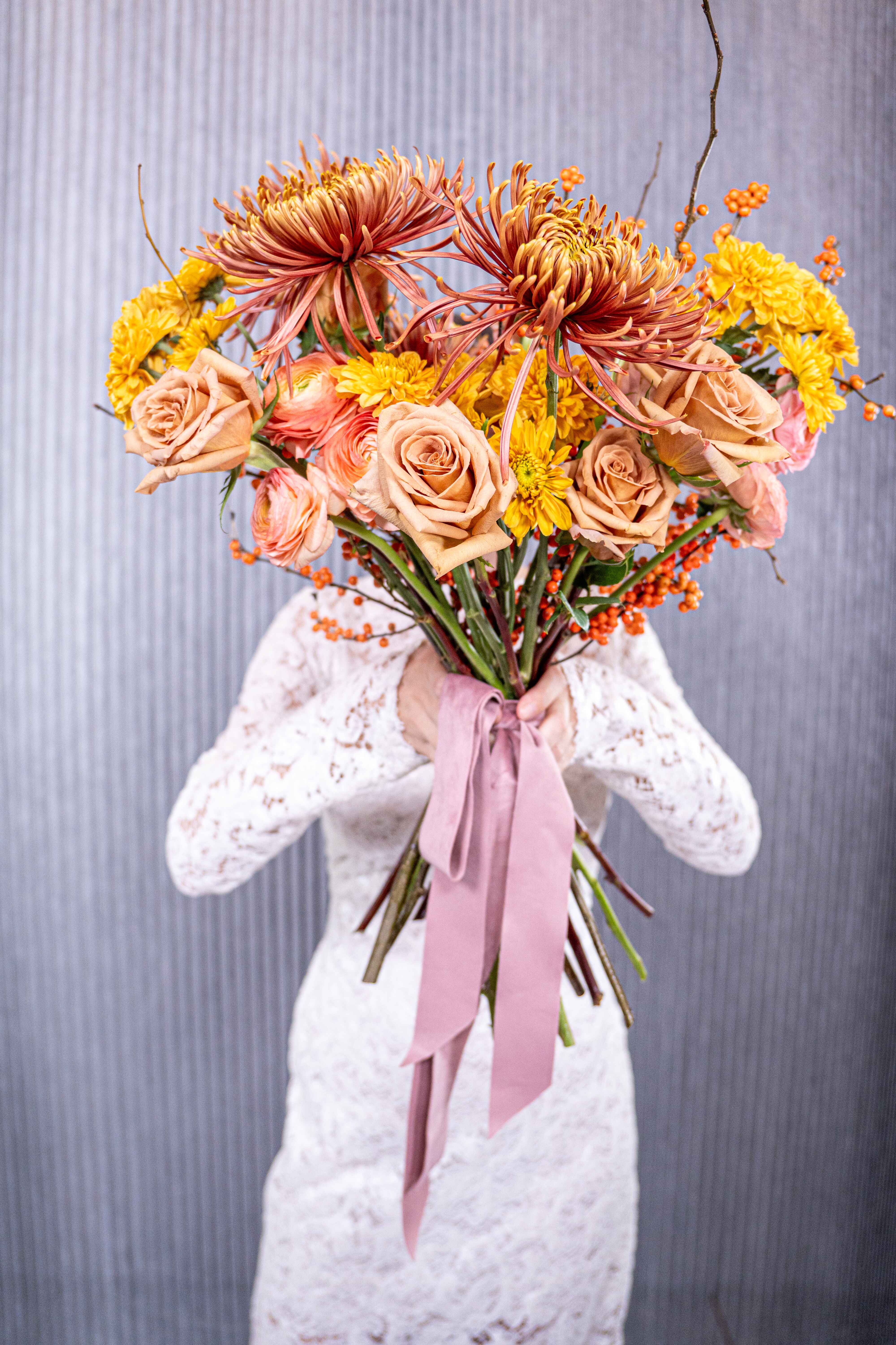 №207 Golden Fall - “Golden Fall” is a stunning tribute to the warm, earthy hues of autumn. This bouquet beautifully captures the essence of the season with a vibrant combination of golden-yellow chrysanthemums, soft peach roses, and bold orange ranunculus. Each bloom radiates warmth, while the burnt orange spider mums add a unique, textured element that brings depth and drama to the arrangement. Delicate orange berry branches further enhance the bouquet’s seasonal charm, adding a playful yet elegant touch. The harmonious blend of rich colors and varied textures mirrors the changing leaves and crisp air of fall, creating a sense of coziness and natural beauty. Whether it’s an autumn wedding, a seasonal gathering, or a thoughtful gift, “Golden Fall” brings the spirit of autumn to life, embodying both elegance and the raw beauty of nature’s transformation during this time of year. This bouquet is more than a floral arrangement; it’s a vibrant reflection of fall’s radiant splendor.