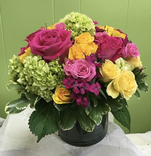 Our Blossoms in Vogue Our Blossoms in Vogue - Brilliant green hydrangea, hot pink and bi-color roses, hot pink and yellow spray roses and greens are hand-delivered in stunning style: a wide cylinder vase that's been elegantly lined with leaves. This bouquet is a singular sensation! Approximately 13" W x 12" H