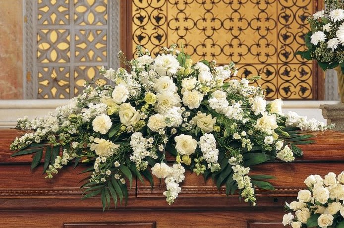 Pure White Casket Spray - This casket spray with its array of white carnations, larkspur, asters and stock adds a pure and loving gesture to the service. One casket spray arrives decorated with white carnations, larkspur, lisianthus, asters and stock, and simple foliage.