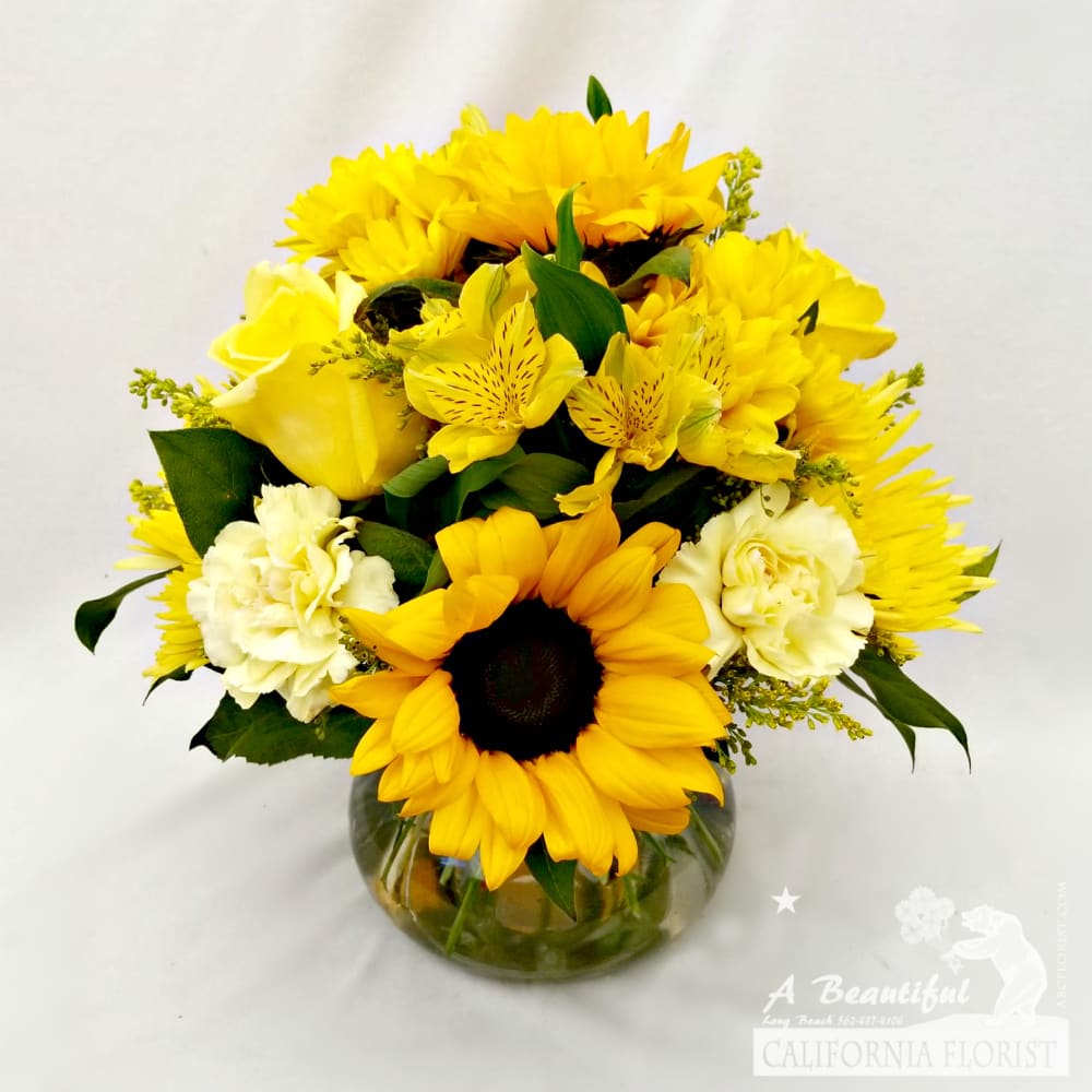 Yellow Posie - Sunshine and Smiles Yellow Posie - Sunshine and Smiles - Beautiful Sunflowers, Roses, Alstroemeria, Carnations and Mums burst forth in yellow positivity! This is the perfect arrangement to send for Get Well, Birthday or Just Because... Approximate size is 8" wide x 12" tall. The type of flowers may change as our artisan house florist creates from the freshest blooms delivered to us from the flower market. But no worries as it will be in absolutely glorious shades of YELLOWs! Order the Yellow Posie today from your local independent, minority woman and family owned Long Beach Flower Shop, A Beautiful California Florist.
