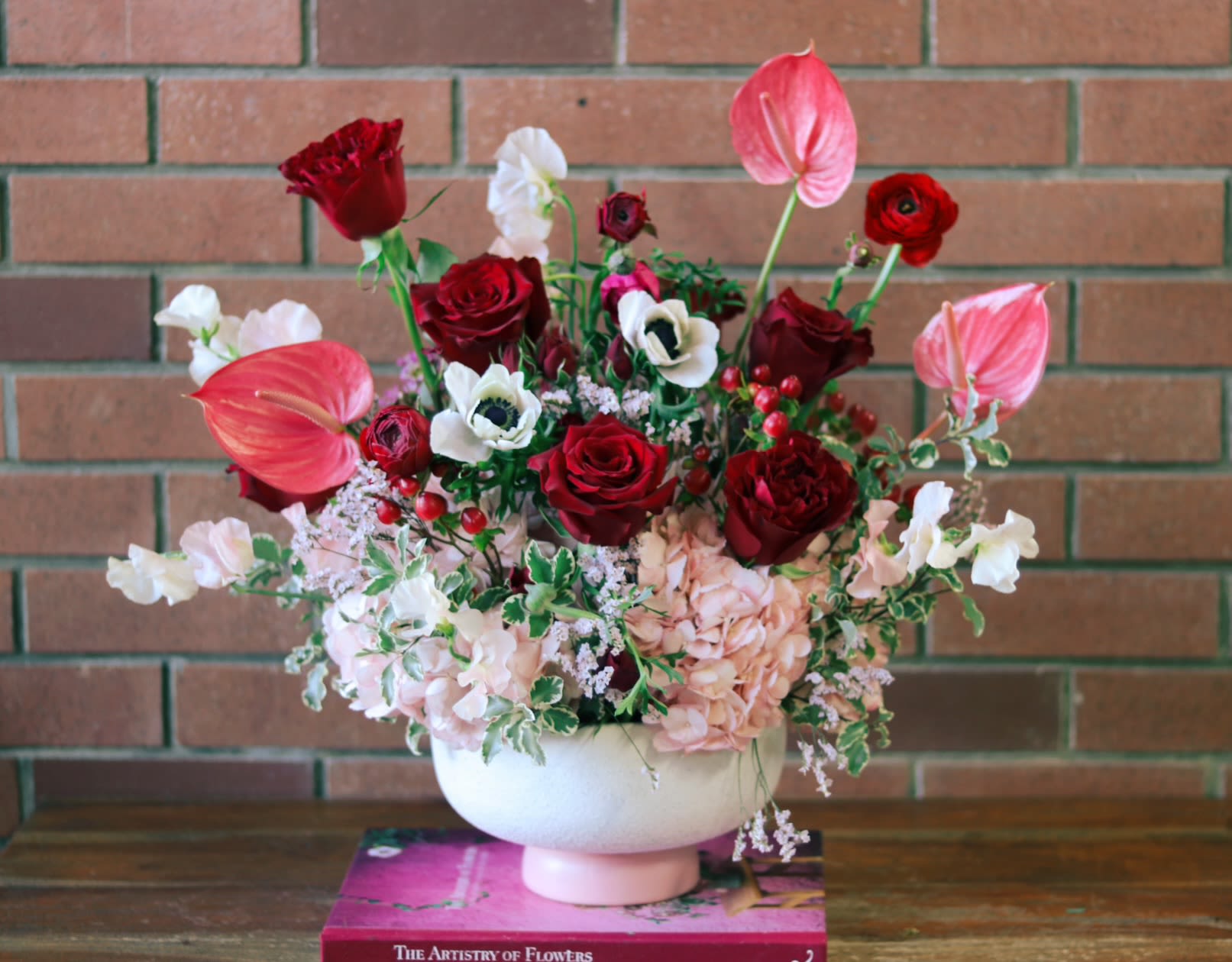 Blossoms Of Devotion Blossoms Of Devotion - Overflowing with rich, romantic colors and lush textures, this captivating floral arrangement from Venetian Flowers is a breathtaking expression of heartfelt love. Sumptuous red and pink panther roses, pink anthurium, pink hydrangeas, fragrant sweet peas, touches of romantic anemones and ranunculus lush and accented with pink hypericum berries, are artfully composed in a modern, striped compote vase - creating a stunning visual that commands attention. The abundance of blooms symbolizes the depth of your affection, while the varied hues of red and pink evoke the passionate, all-encompassing nature of your devotion. Every thoughtfully-placed stem radiates an air of elegance and refinement, making this arrangement a stunning centerpiece that will leave a lasting impression on your Valentine. Crafted with the utmost care by the skilled designers at Venetian Flowers, "Blossoms of Devotion" is a masterful representation of floral artistry. This truly special creation will convey the fullness of your heart in the most beautiful, heartfelt way. Give the gift of romance that will be cherished for days to come.