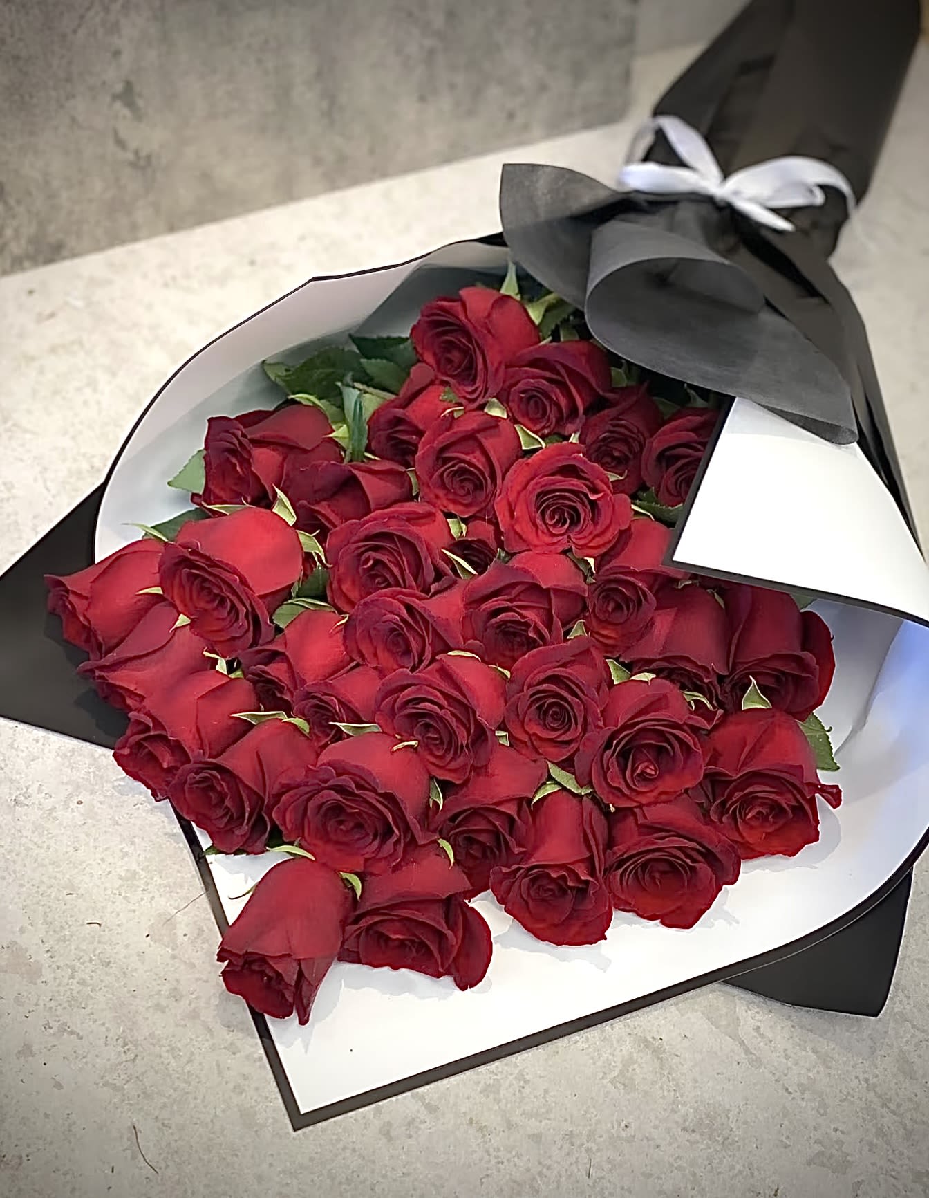 Scarlet Embrace -  Scarlet Embrace – The Ultimate Symbol of Love   Nothing speaks of passion and romance like a bouquet of luxurious red roses. Scarlet Embrace is a breathtaking arrangement, elegantly wrapped in black and white, creating a striking contrast that enhances its beauty. This stunning bouquet is designed to leave a lasting impression on the one you love.   Perfect for:  Romantic surprises – Say “I love you” in the most timeless way.  Special occasions – Anniversaries, birthdays, or proposals.  Grand gestures – Because love deserves to be celebrated in style.  Make your moments unforgettable with Scarlet Embrace. Order now and let love bloom! ️