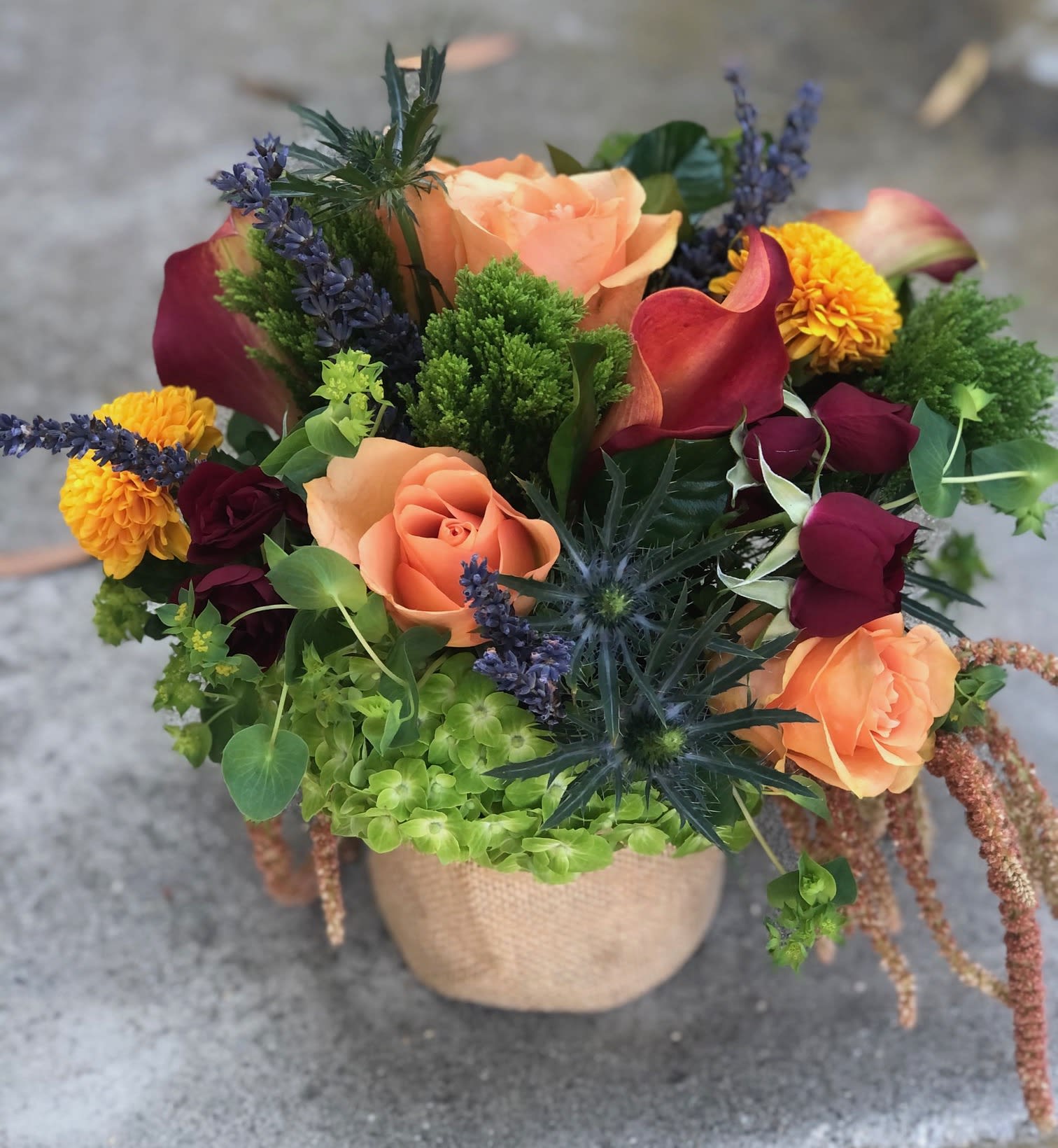 Fall Garden - A vibrant and colorful arrangement full of a variety of flowers and textures all set off by lush green hydrangea and velvety green notes presented in a burlap covered glass vase all accenting the richness of fall.