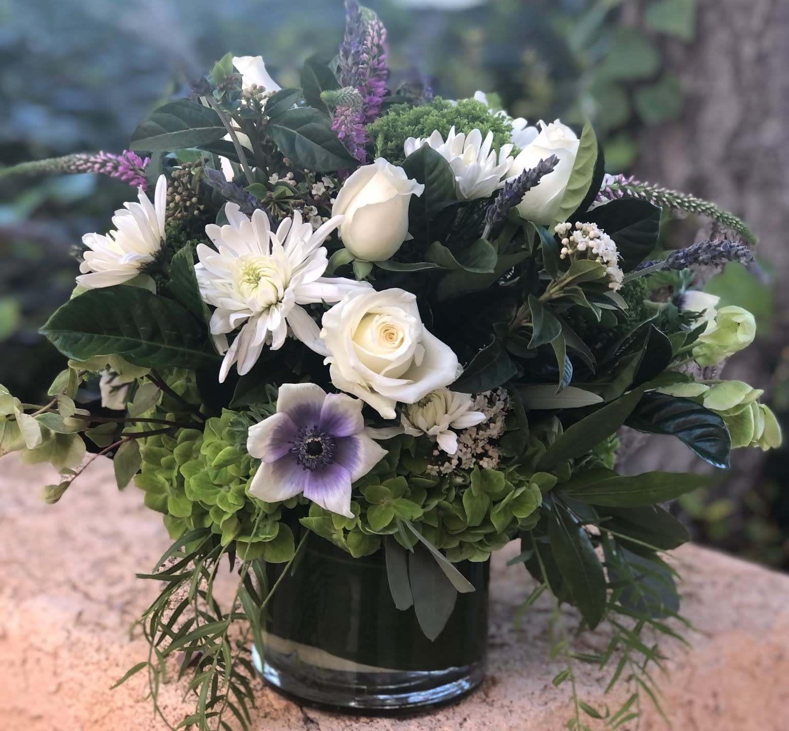 MacKenzie's Meadow - Green and white lush arrangement with accents of purple and lavender. Chunky clover  hydrangea with accented with textures such as fresh lavender, pepper berry, seeded eucalyptus, gardenia foliage and velvety dianthus all highlighting garden flowers such as roses, ranunculus, anemone and veronica.  Perfect for as a gift for birthday, spring, Mother's Day or St Patrick's Day!