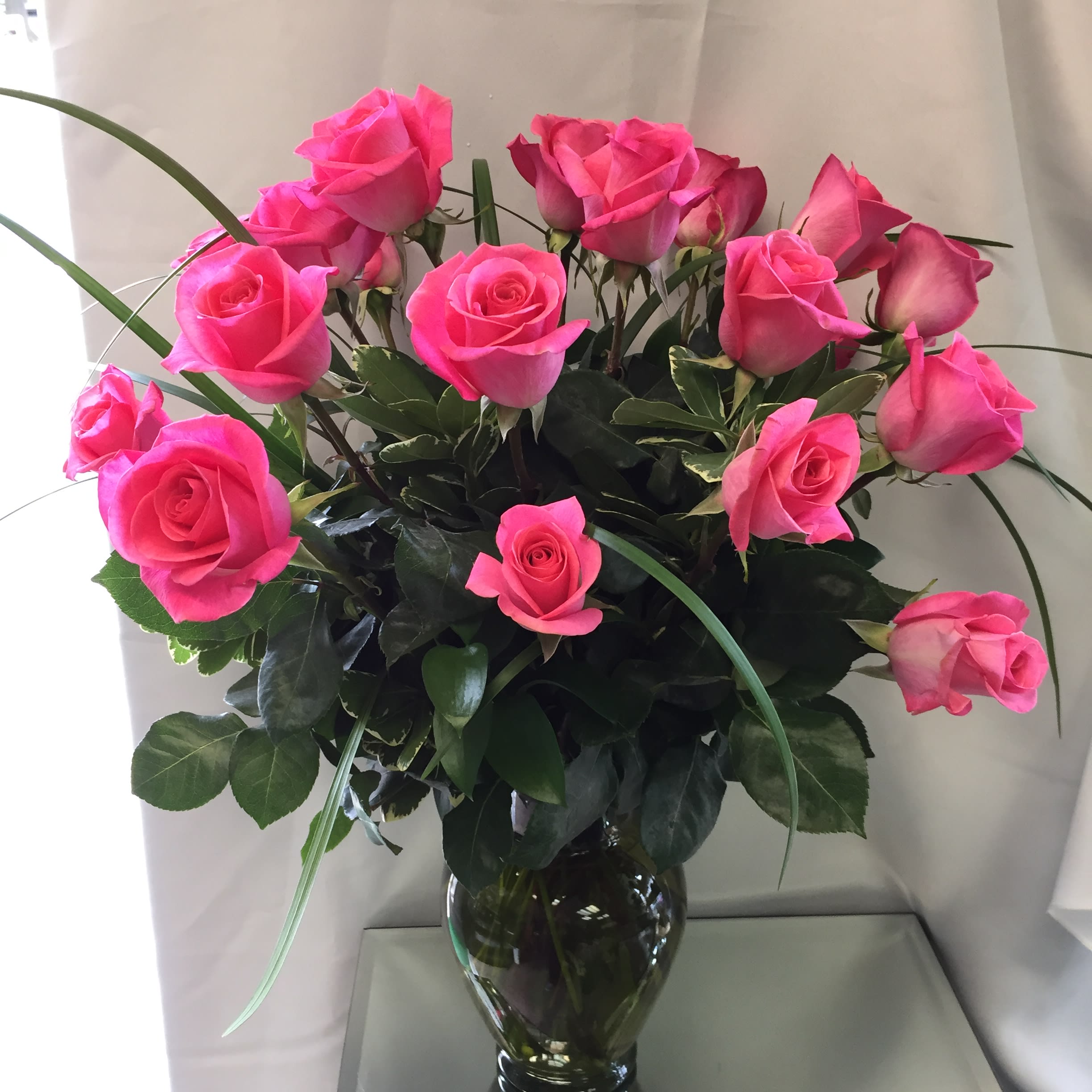 Pink Rose Rhapsody - Deep pink roses arranged in a glass vase - a mix of foliage makes for a chic style.