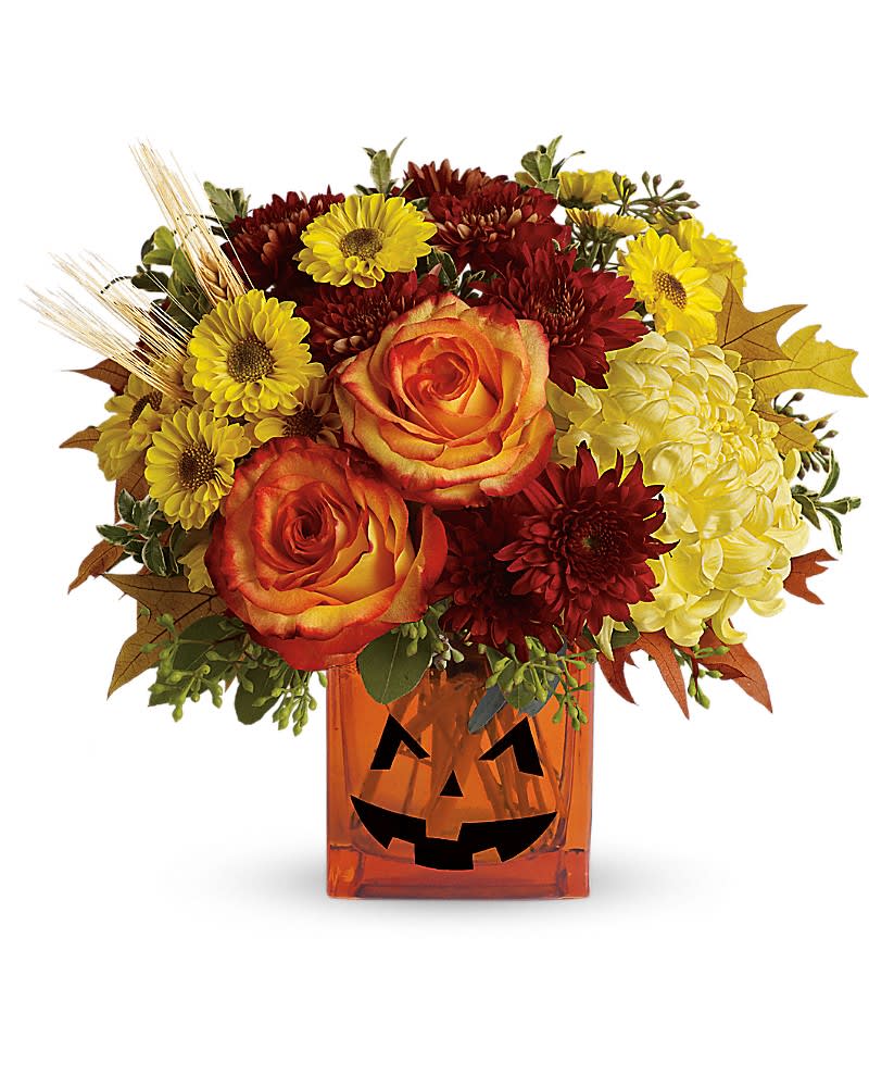 Teleflora&#039;s Halloween Glow - As colorful as Halloween candy! Yellow chrysanthemums are accented with bright orange roses and finished with eucalyptus and autumn oak leaves. All in an orange cube adorned with a jack-o-lantern face that&#039;ll brighten and frighten! This bright bouquet includes yellow cushion spray chrysanthemums, bi-color orange roses, rust cushion spray chrysanthemums, yellow disbud chrysanthemums, yellow viking spray chrysanthemums, oregonia, eucalyptus and autumn oak leaves. Delivered in an orange cube vase.