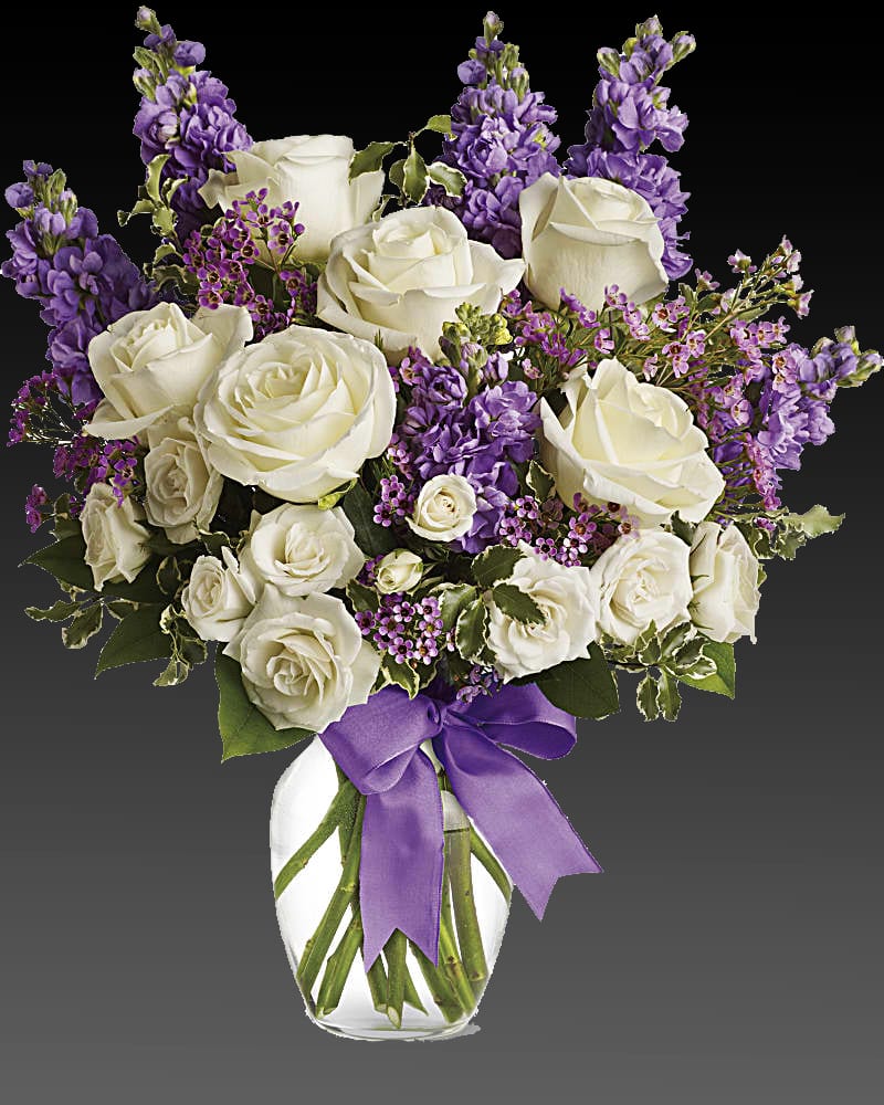 Enchanted Cottage Bouquet - As enchanting as coming across a hidden cottage in the countryside! Lush white roses and purple stock mix with delicate lavender waxflower and green pitta negra for an elegant English garden look. The decorative bouquet is finished with a pretty satin ribbon. White roses meet lavender stock and waxflower in this lush, elegant arrangement. Presented in a classic clear glass vase with purple satin ribbon. Orientation: One-Sided