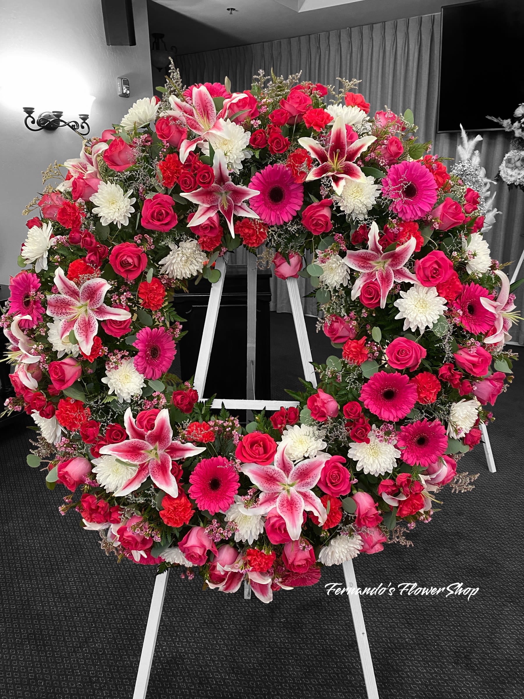 Thoughts  - A stunning floral wreath featuring pink stargazer lilies, vibrant roses, gerbera daisies, carnations, and white chrysanthemums. This beautiful arrangement symbolizes love, admiration, and heartfelt remembrance. Perfect for honoring a cherished life.  COLOR CAN BE CHANGE AT NO EXTRA COST