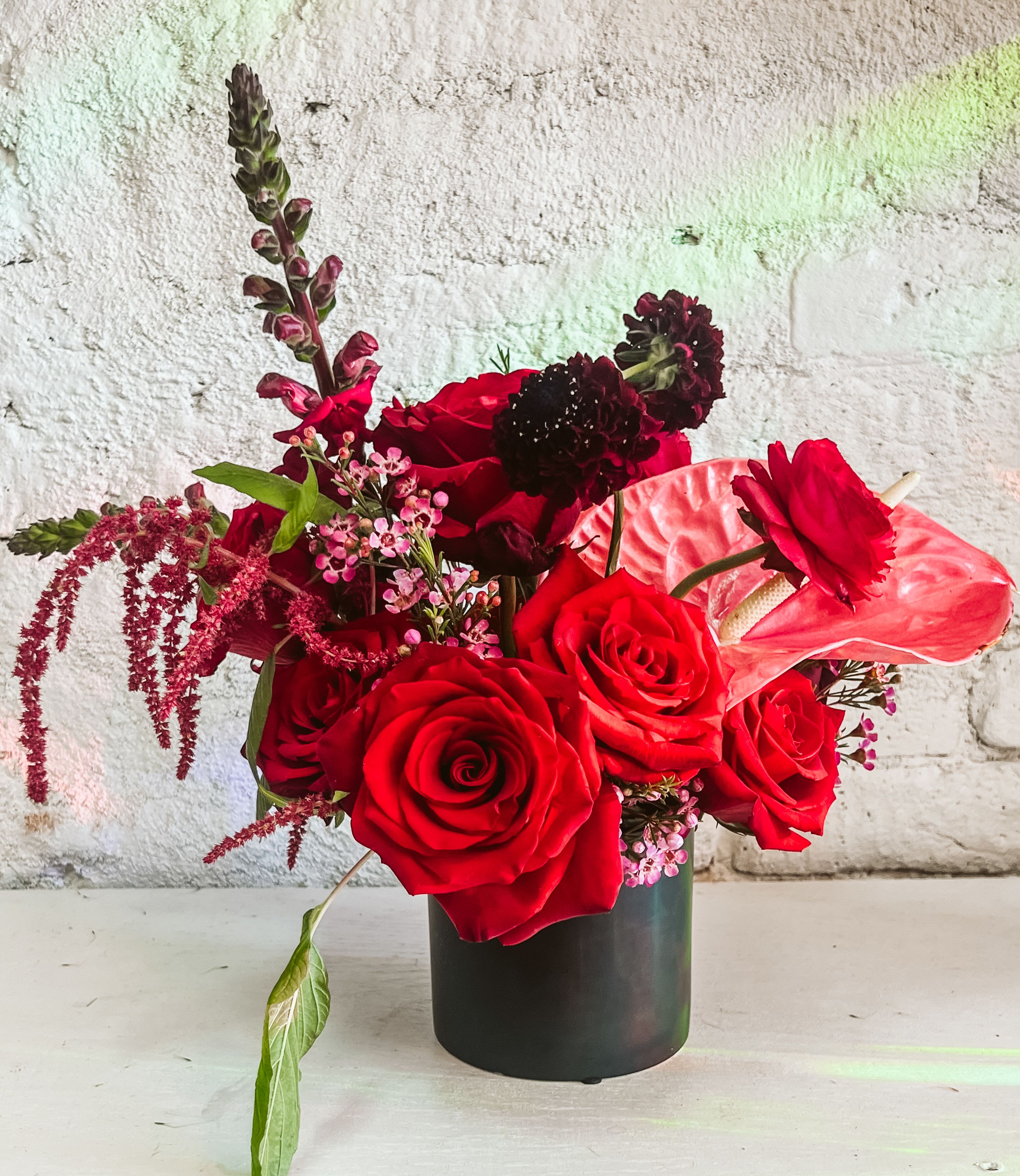 Romance Special Order - This exquisite arrangement is thoughtfully crafted to express love and beauty in the most heartfelt way. We’ve meticulously hand-selected the finest blooms to create a design that speaks volumes. Featuring vibrant pink ranunculus, lush red roses, delicate pink anthurium, cascading red hanging amaranthus, rich burgundy scabiosa, snapdragons, and charming wax flowers, this masterpiece captures the essence of the season. Overflowing with elegance and passion, it’s a striking expression of love that will leave a lasting impression.  *some varieties and colors may vary depending on availability. Any and all bloom replacements will be of equal visual presence and value. 