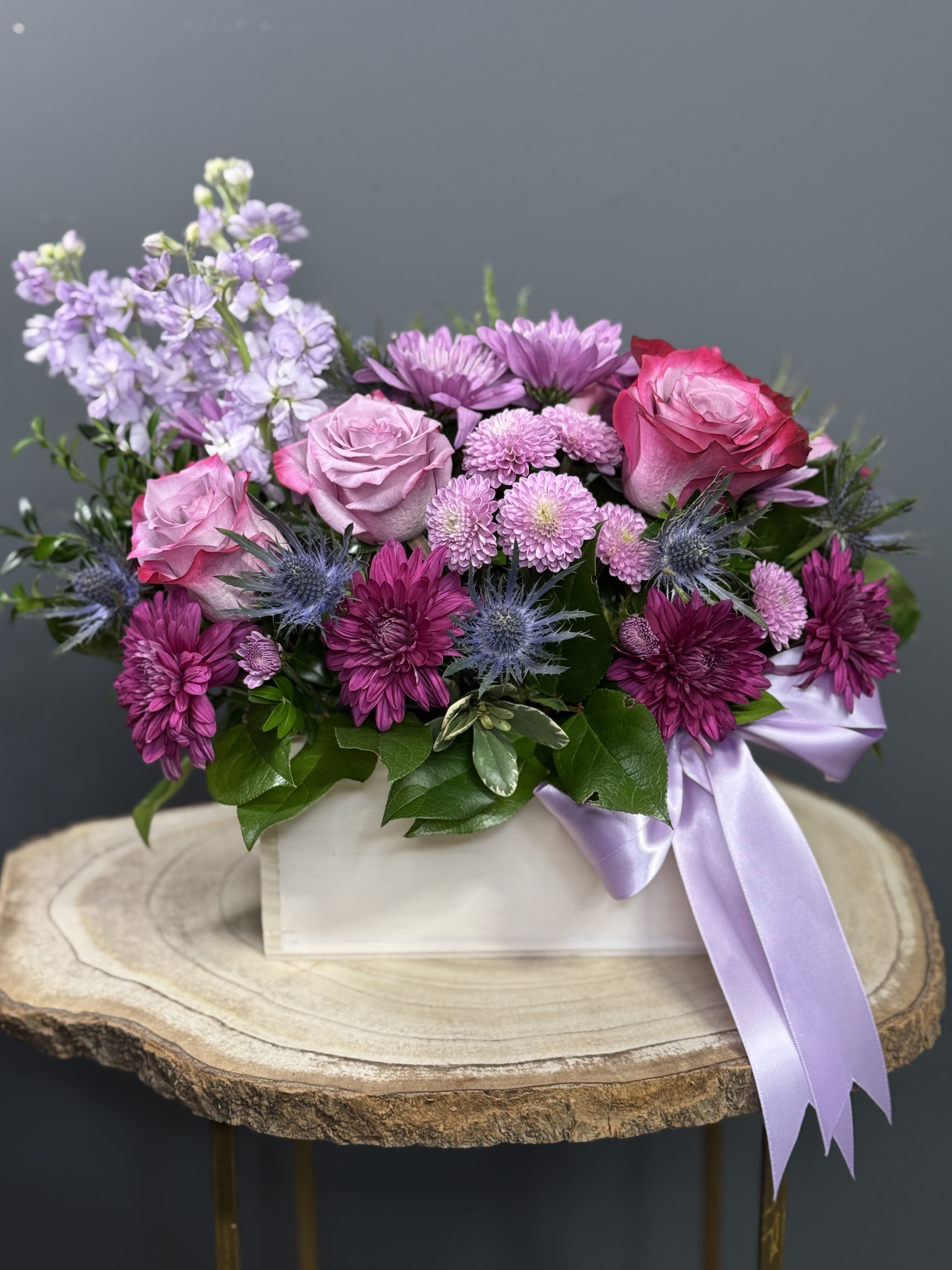 Lavender Fields - Lavender Fields is a mesmerizing floral arrangement that embodies the serene beauty of lavender. This design exudes tranquility, featuring delicate lavender roses and blooms artfully arranged in a charming white-washed box. Adorned with a soft lavender satin ribbon, this arrangement is a perfect blend of natural grace. Ideal for expressing love, calmness, and admiration, &quot;Lavender Fields&quot; is a thoughtful gift suitable for any occasion, promising to bring joy and serenity to its recipient.