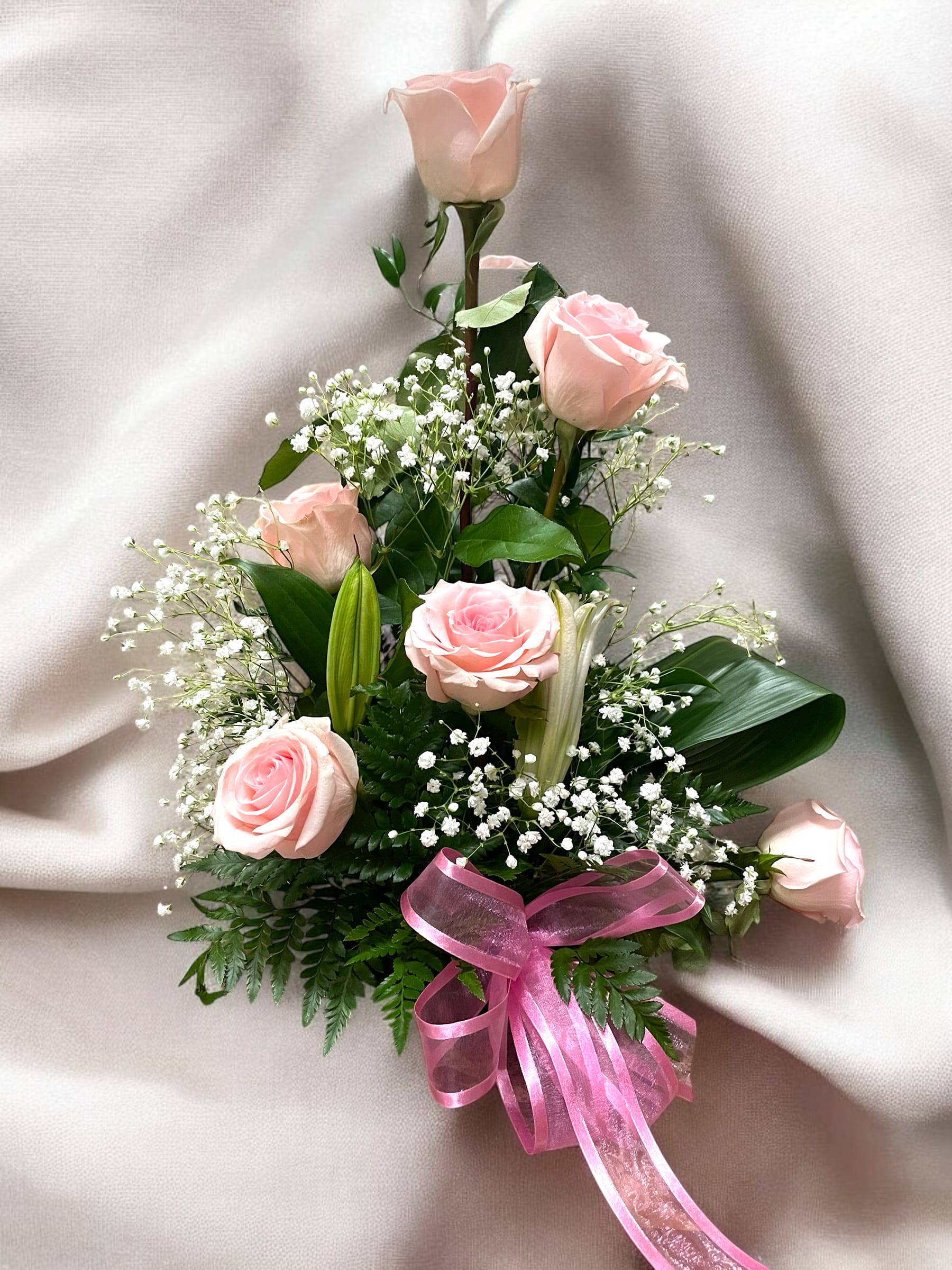 Blushly Blushly - Soft pink roses, complemented by delicate baby's breath, lush green foliage, and the pink ribbon, give it a graceful and romantic touch. Perfect for occasions like weddings, anniversaries, or expressing heartfelt sentiments.