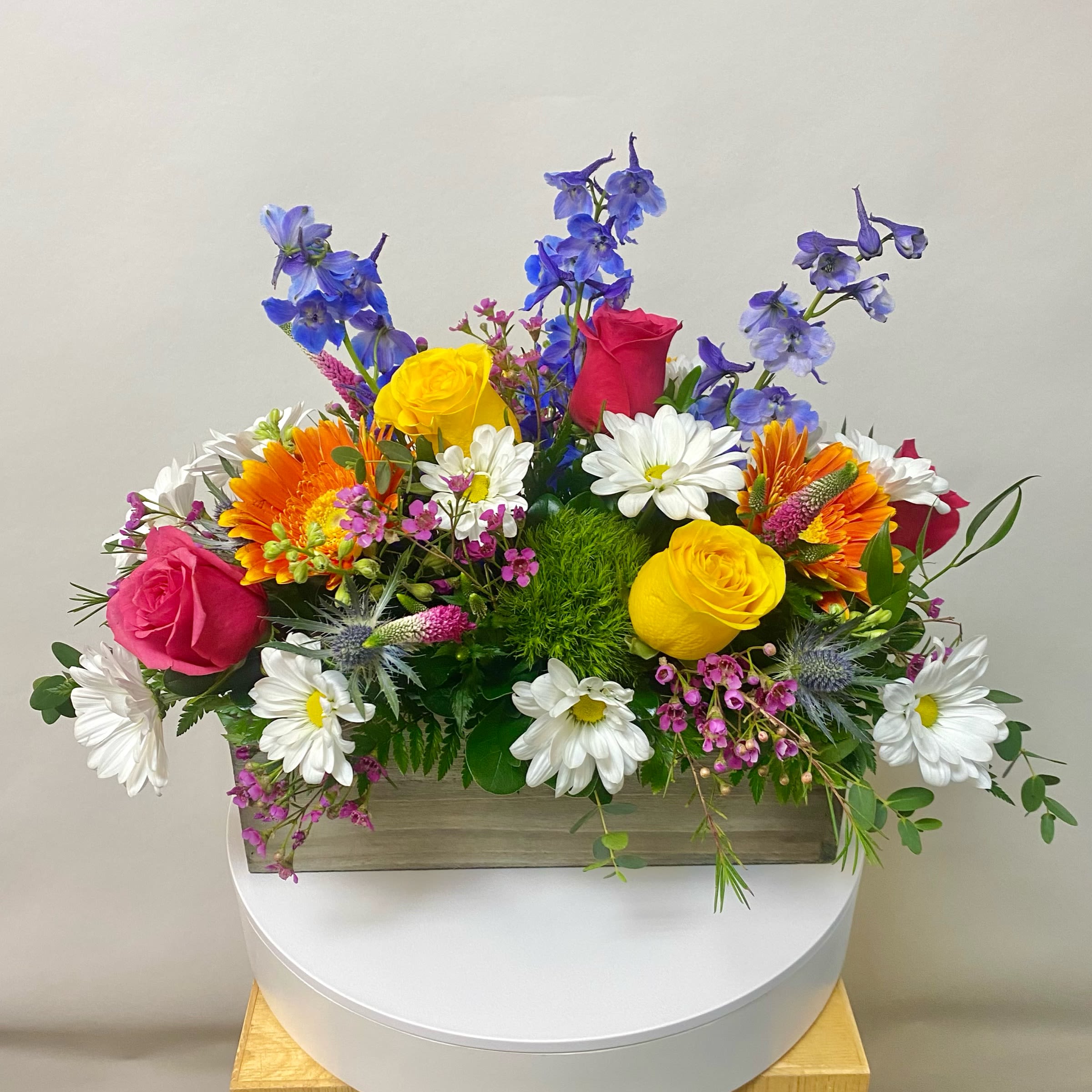 Wildflower Box - This Wildflower Wooden Box Arrangement includes Hot Pink Roses, Yellow Roses, Orange Gerbera, Blue Delphinium, Green Dianthus, White Daisies, Hot pink of Purple Veronica and Blue Thistle. Or as Similar as Possible. 