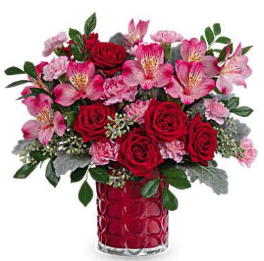 Enchanted Hearts Bouquet - Adorned with a charming heart pattern and gleaming with a pearlescent finish, this delightful glass vase adds an extra touch of magic to their Valentine's Day when filled with a stunning red and pink bouquet. This Valentine's Day arrangement features red spray roses, pink alstroemeria, and miniature light pink carnations, complemented by dusty miller, seeded eucalyptus, and huckleberry. This vibrant red and pink bouquet is delivered in Teleflora's Enchanted Hearts Vase (while supplies last).