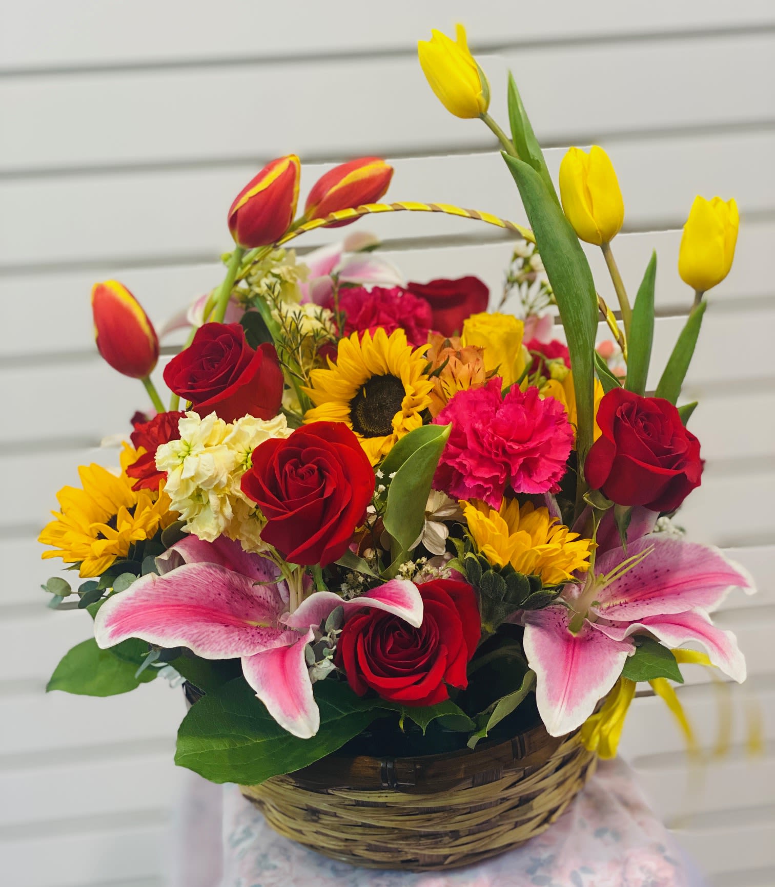 Bright and Cheerful Basket - Featuring lilies, tulips, roses, Sunflower, carnation, and more in a Bright and colorful basket arrangement. Short of a pollen allergy, this is as close to gifting a season you can get. Perfect for all type of gift, this arrangement will be sure to impress. 