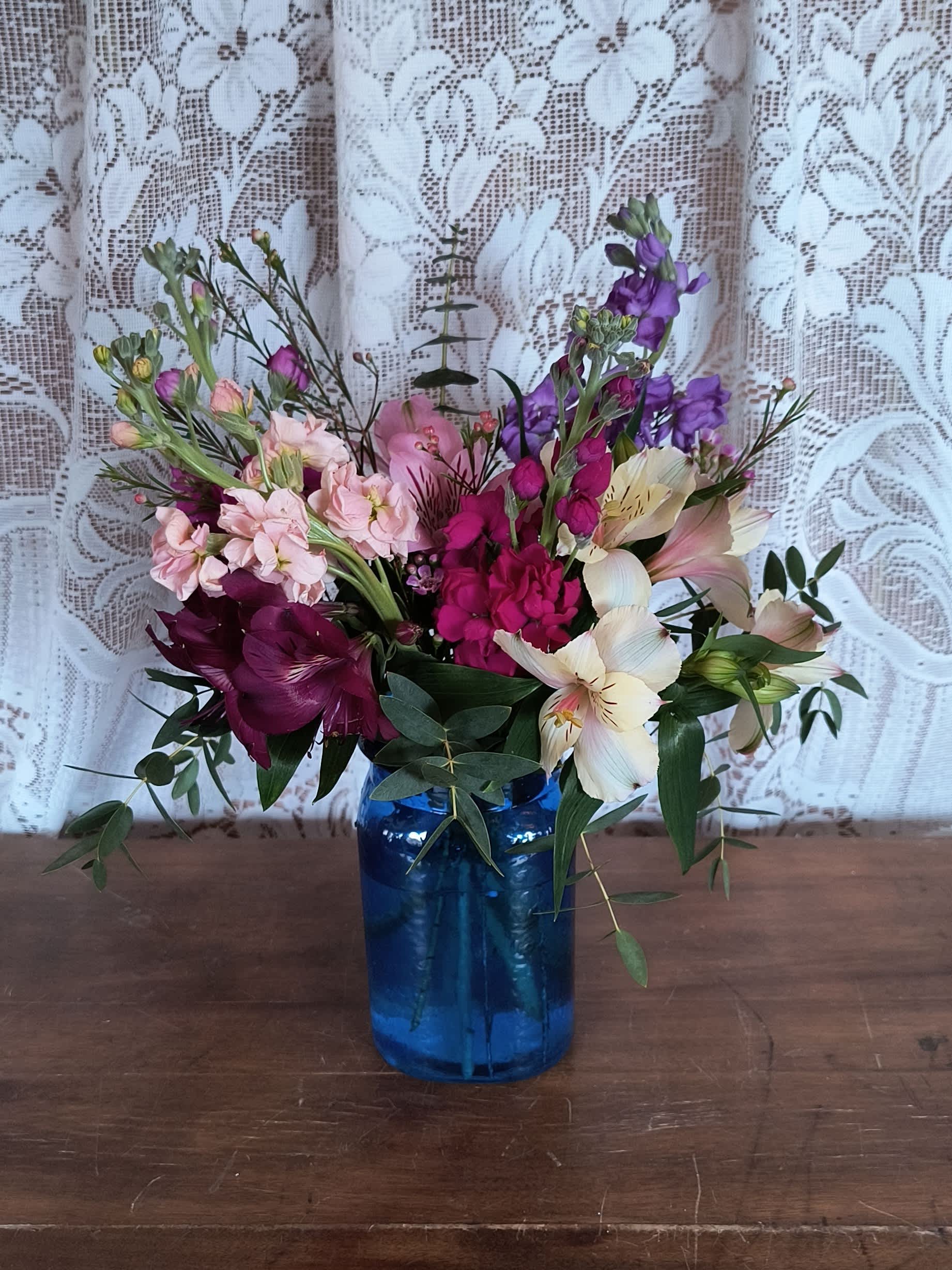 Jewels - A colorful jewel tone mix of stock and alstroemeria with eucalyptus and wax flower arranged in a cobalt blue vase. Content colors may vary.