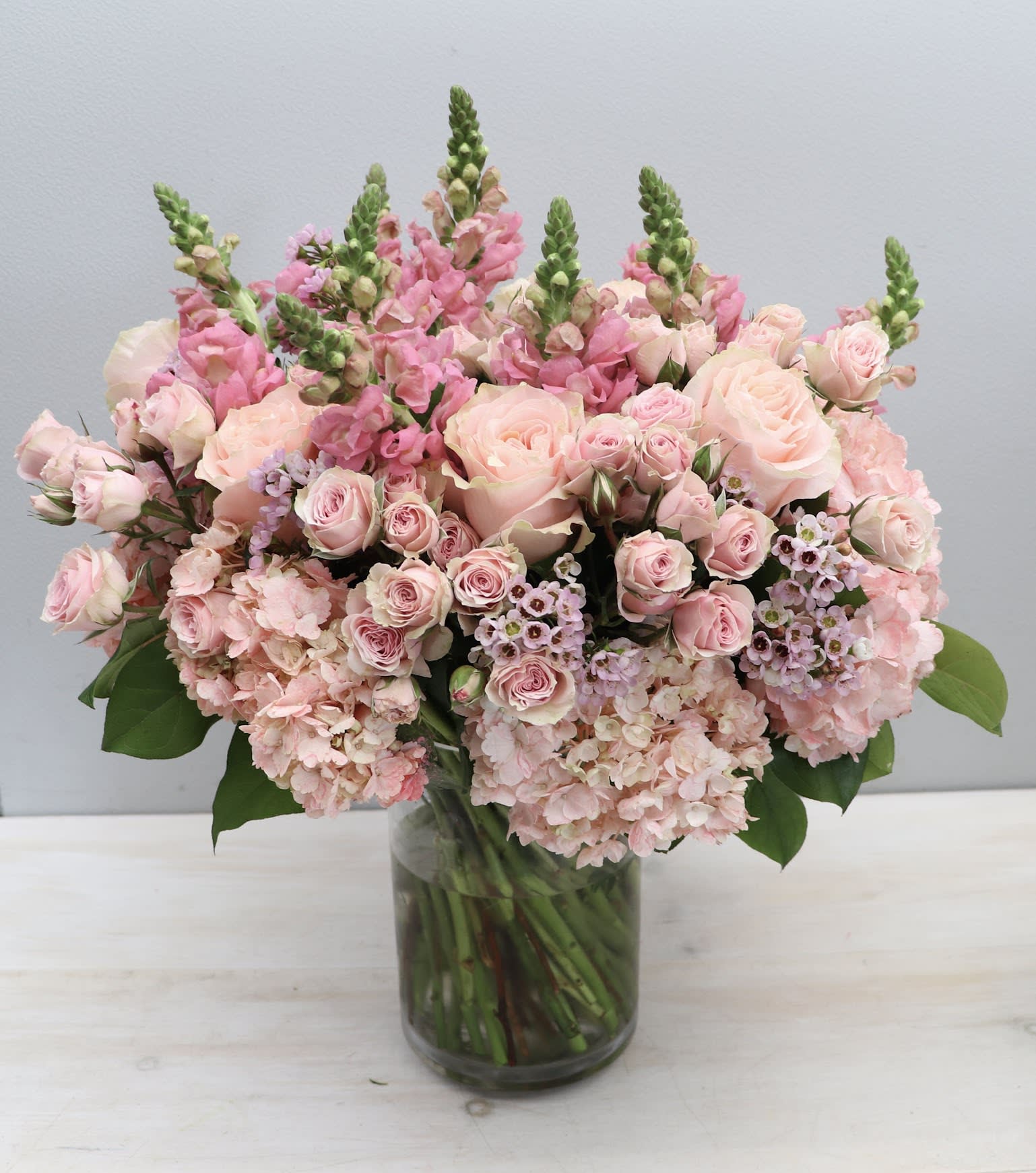 Spring Sunset - WeHo Spring Sunset - WeHo - This monochromatic look includes hydrangea, roses, snapdragons, and a mix of seasonal greenery to achieve it's overall look. The photo displayed is in the standard size, the standard size stands at about 15-20 inches tall and wide. Don't forget to upgrade for more blooms.