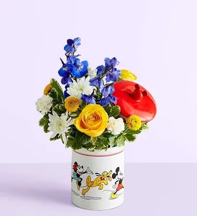Disney Mickey Mouse &amp; Friends Cookie Jar- Baby Boy - EXCLUSIVE Welcome the little prince with a gift full of character(s)! Part of our new Disney collection, this handcrafted bouquet is gathered in happy yellow, blue and white blooms and designed in our whimsical Mickey Mouse and Friends cookie jar, featuring iconic animations. Great as a keepsake container or for keeping treats, it’s an adorable way to celebrate the littlest Disney fan and family. All-around arrangement with yellow roses and button poms, white mini carnations and cushion poms, blue delphinium; accented with assorted greenery Artistically designed in our exclusive Mickey Mouse and Friends Cookie Jar; food safe container that can be used as a keepsake or for any type of treat once the flowers have expired; measures 7.5&quot;H x 4.5&quot;D