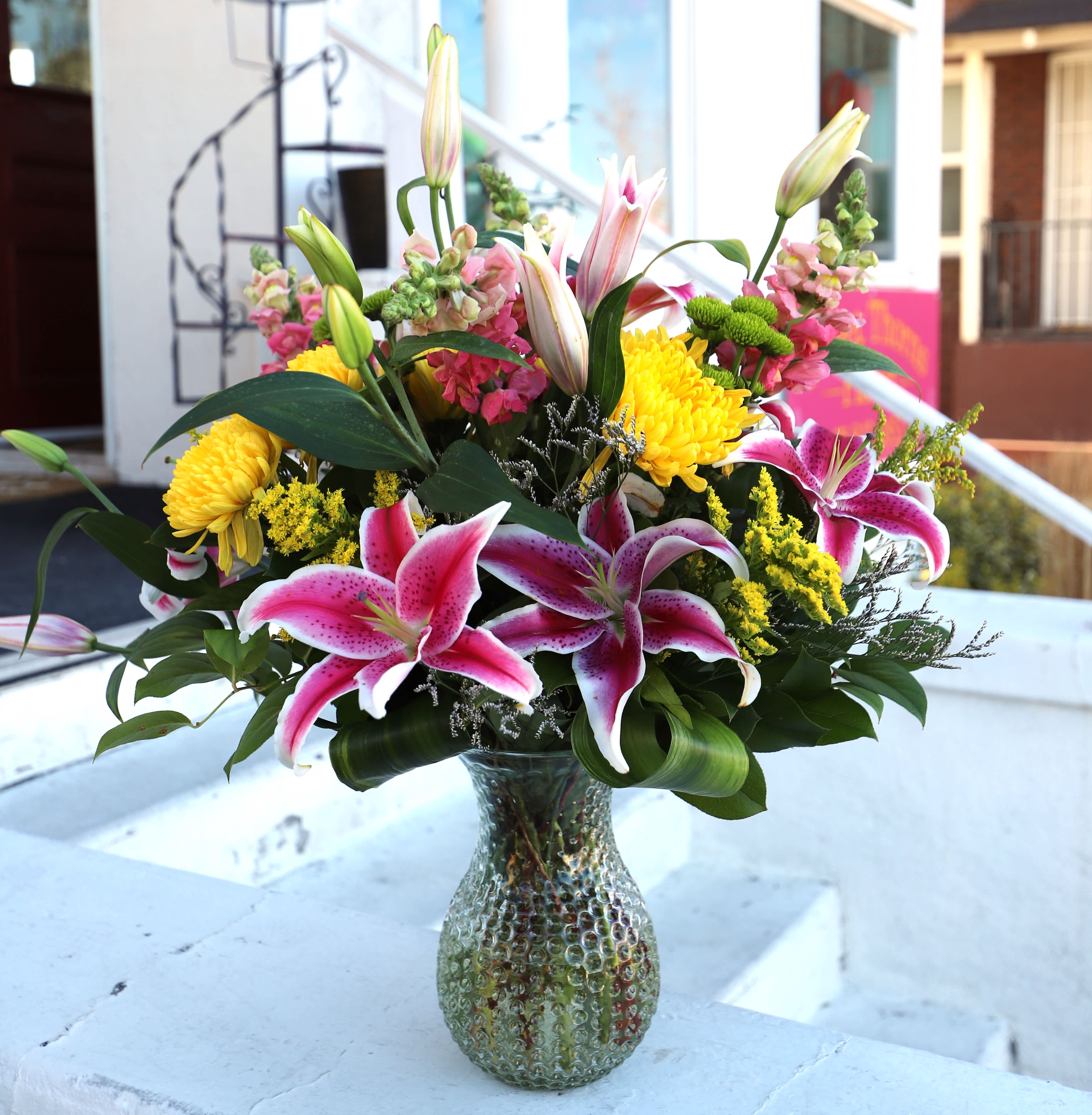 Together Forever - A stunning floral arrangement made in a fun textured vase with brightly colored chrysanthemums, lilies, snapdragons, and other filler flowers and greenery.