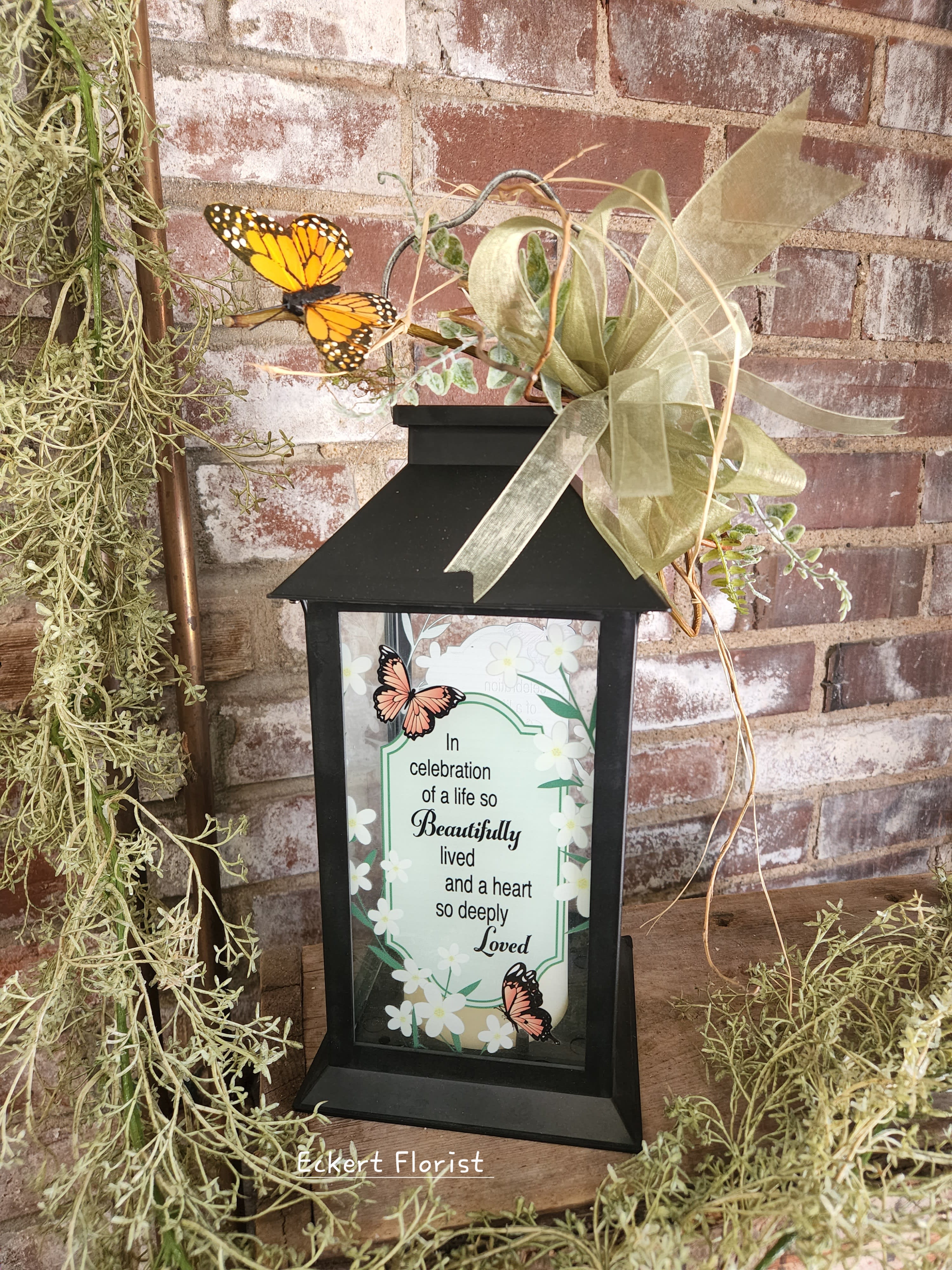 Eckert Florist's Butterfly Lantern Eckert Florist's Butterfly Lantern - **Our Local Delivery Only Molded lantern measures approx. 11" H X 5.5" Square. Sentiment: "In celebration of a life so Beautifully lived and a heart so deeply Loved." Adorned with a bow and whimsical butterfly, this keepsake lantern with battery operated candle will last for years.