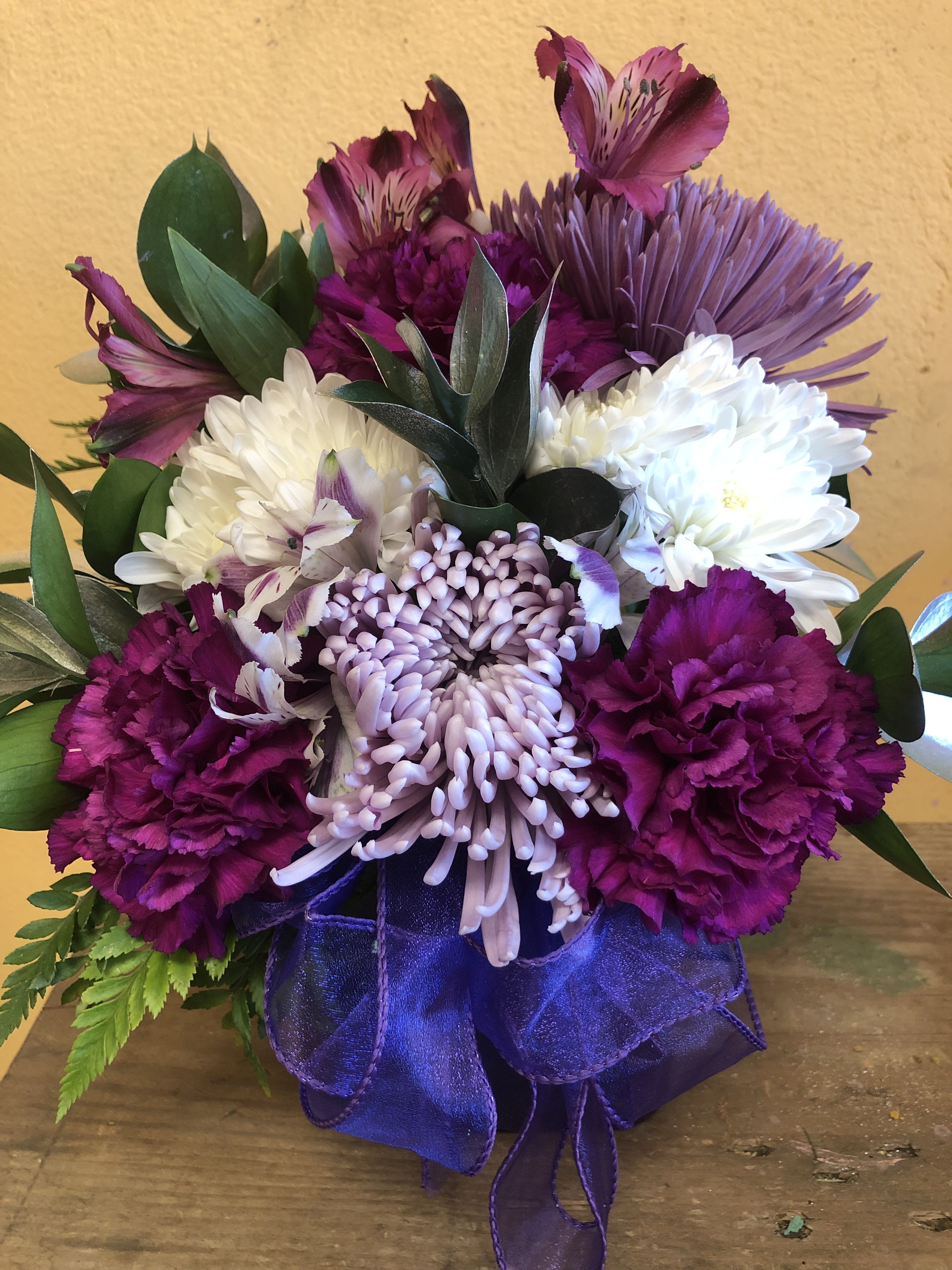 PURPLE AND WHITE CUBE (DESIGNER CHOICE) PURPLE AND WHITE CUBE (DESIGNER CHOICE) - THIS IS A CUBE ARRANGEMENT WITH ALL PURPLE AND WHITE FLOWERS TO INCLUDE CARNATIONS, CUSHION, ALSTROMERIA AND SPIDERS. FILLERS WILL BE EITHER GOLD OR SILVER RUSCUS. NOTE THIS ARRANGEMENT DOES NOT INCLUDE ROSES OF LILIES. DELUXE AND PREMIUM PRICE WILL ONLY INCLUDE MORE OF THE MENTION FLOWER BUT IT WILL NOT INCLUDE ROSES OR LILIES