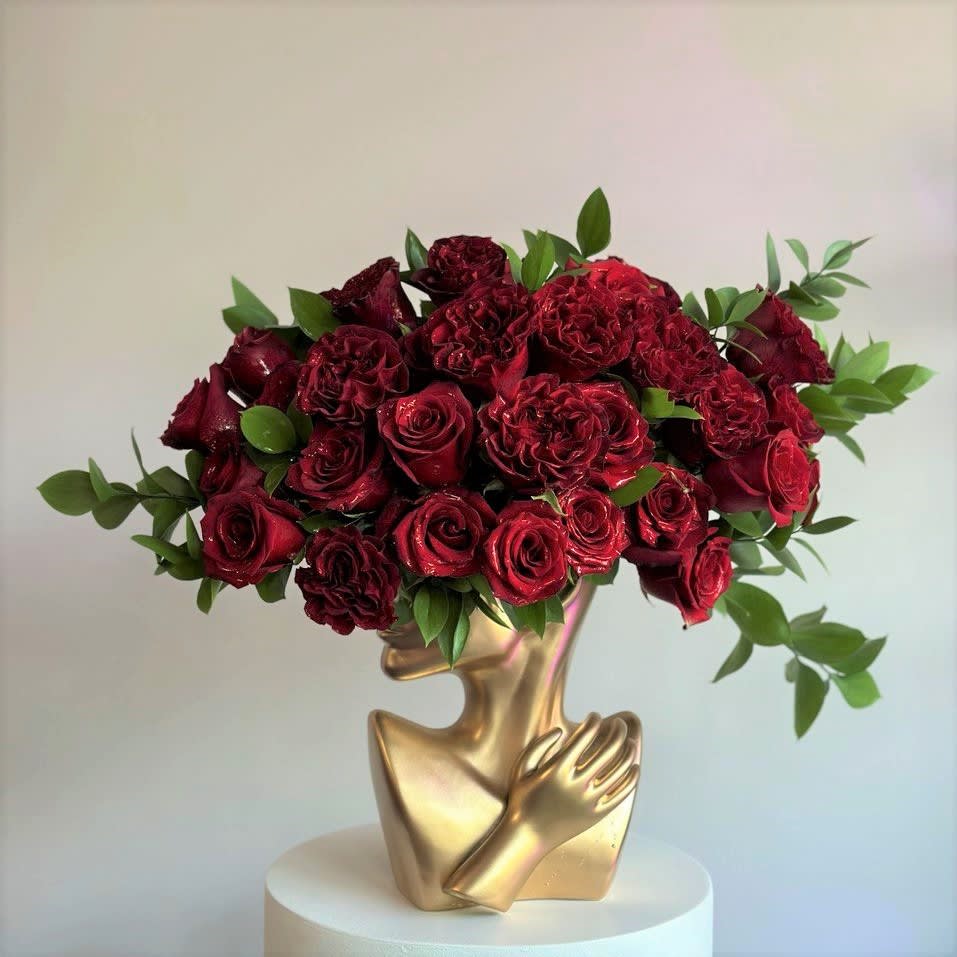 35- Elsa LOVE - This striking red floral arrangement features lush red roses paired with fresh greenery, arranged in a unique gold vase shaped like a woman’s face. The roses cascade beautifully to resemble her &quot;hair,&quot; adding an artistic and elegant touch. The combination of deep reds and the gold accent creates a luxurious and sophisticated centerpiece, perfect for making a bold statement in any space. Ideal for romantic gestures or high-end events. Deluxe size is shown on the pictures