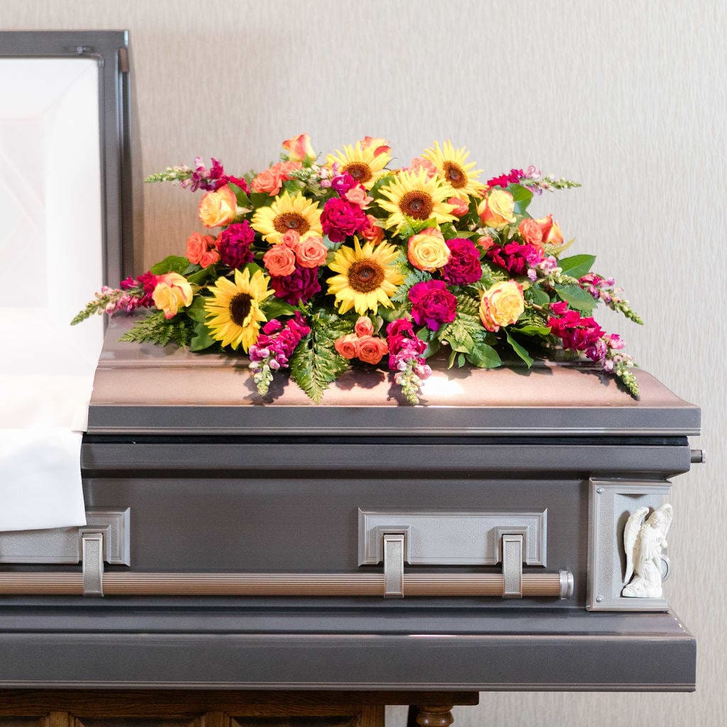 Vibrant - Colorful and eye catching sunflowers and snapdragons, in a casket spray to celebrate a one of a kind life.  Approximate Dimensions: 40&quot;L X 12&quot;T X 24&quot; D