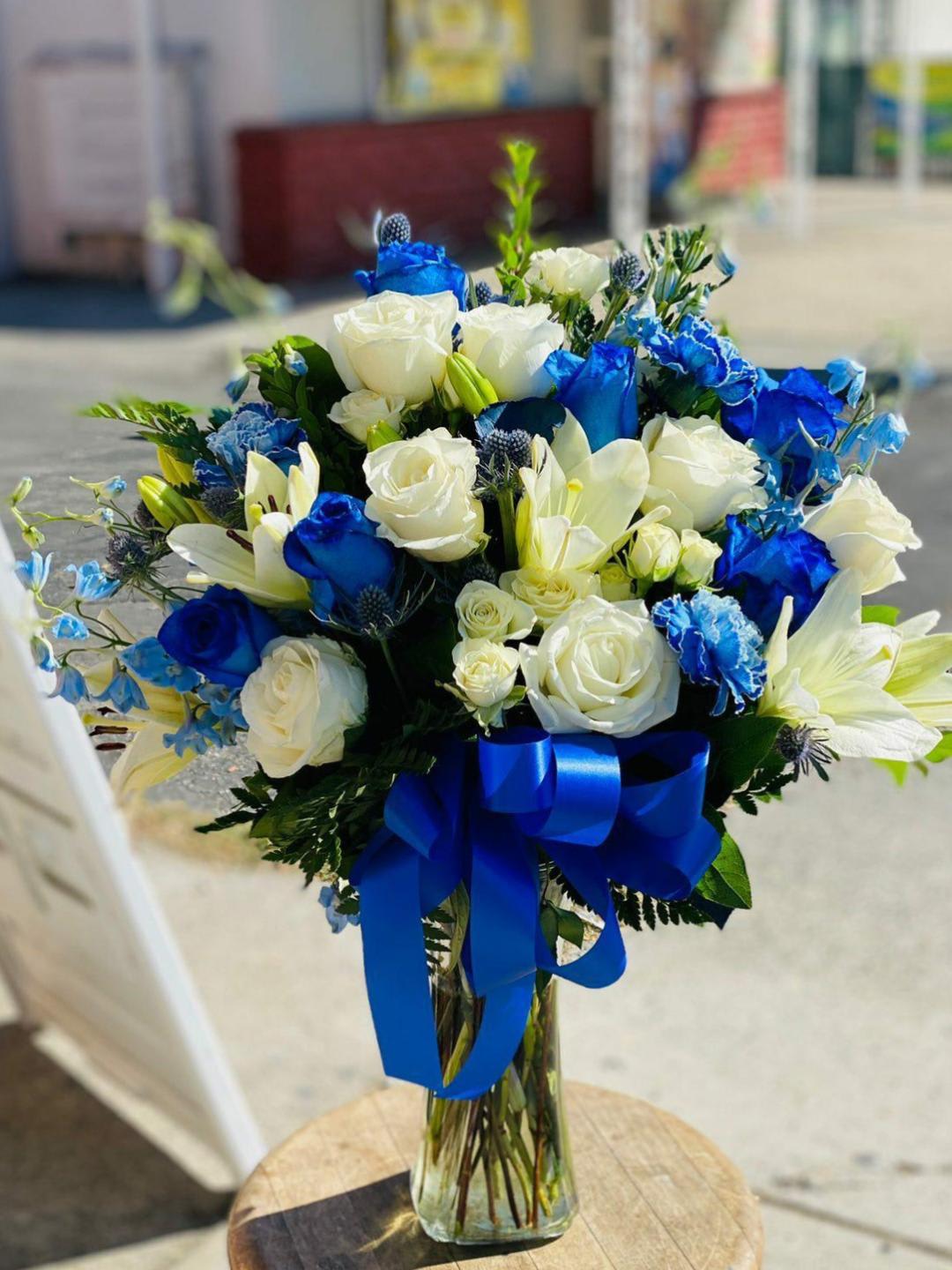 Blue Moon  - Blue roses, white roses, blue carnations, white lilies, with a blue bow. This is a one sided arrangement. 