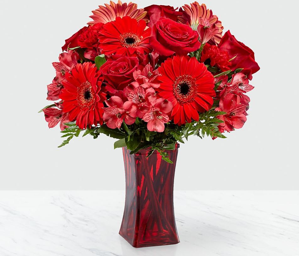 Red Reveal™ Bouquet Red Reveal™ Bouquet - The Red Reveal™ Bouquet bursts onto the scene with a bold beauty that cannot be denied! Ready to celebrate any of life's special moments, this daring bouquet weaves together rich red roses, red gerbera daisies, red carnations, and red Peruvian Lilies with lush greens to create a simply unforgettable gift of flowers. Presented in a modern red glass vase to add to the drama of this arrangement, this flower bouquet is set to send your thinking of you, happy birthday, or, "I love you," wishes across the miles. GOOD bouquet is approximately 14"H x 12"W. BETTER bouquet is approximately 14"H x 13"W. BEST bouquet is approximately 15"H x 14"W.