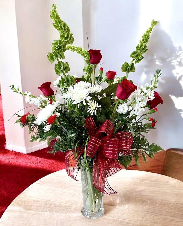 Sleigh Bells Ring Sleigh Bells Ring - Sleigh bells ring! This floral arrangement is presented in a clear glass fluted vase and includes an artistic combination of bells of Ireland, Freedom red roses, white stock, white chrysanthemums, red miniature carnations, and an assortment of mixed winter greenery